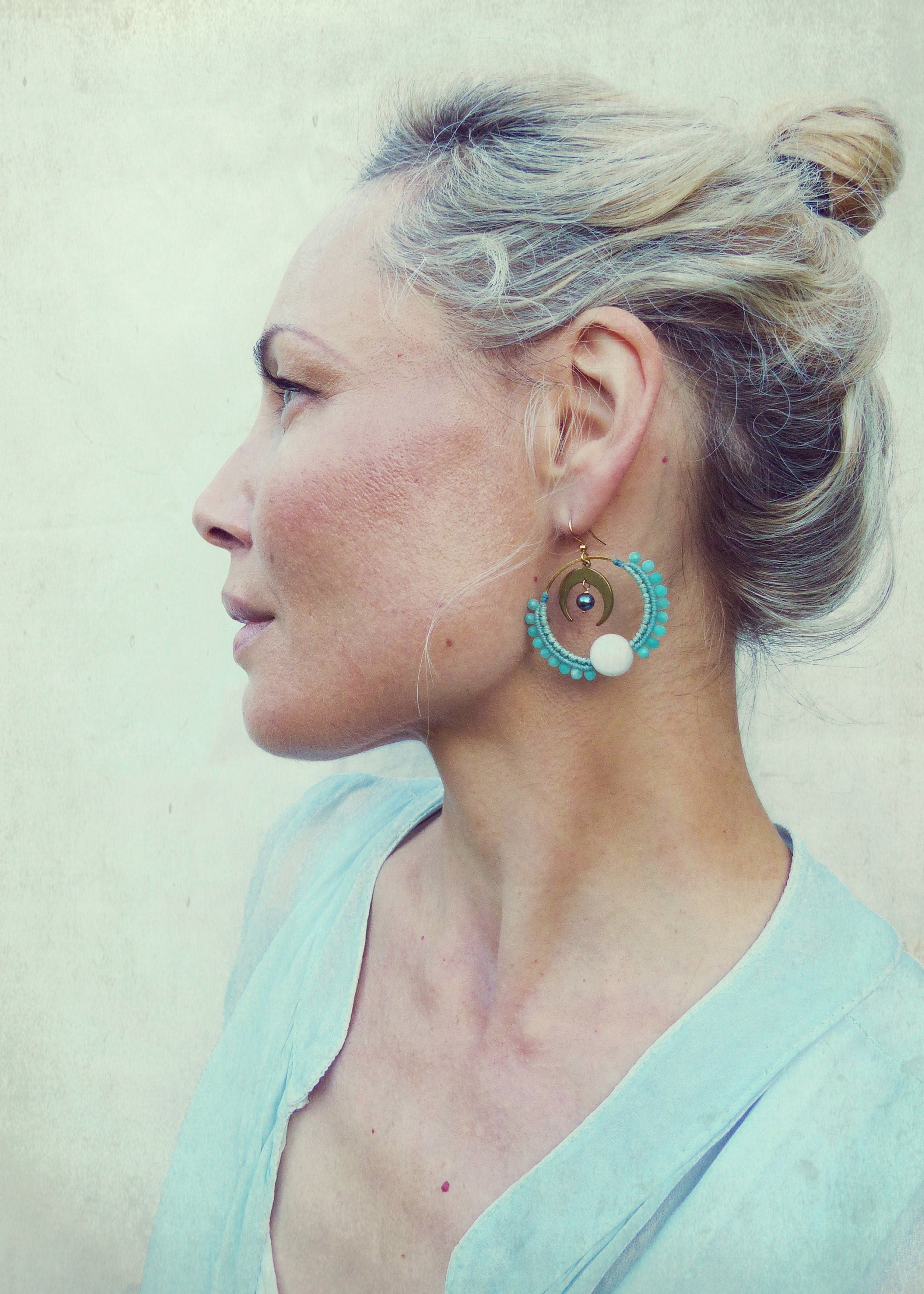 Peut inclure: Une femme portant une chemise bleu clair avec une paire de boucles d'oreilles créoles dorées ornées de perles turquoise et blanches. Les boucles d'oreilles ont un motif de croissant de lune.