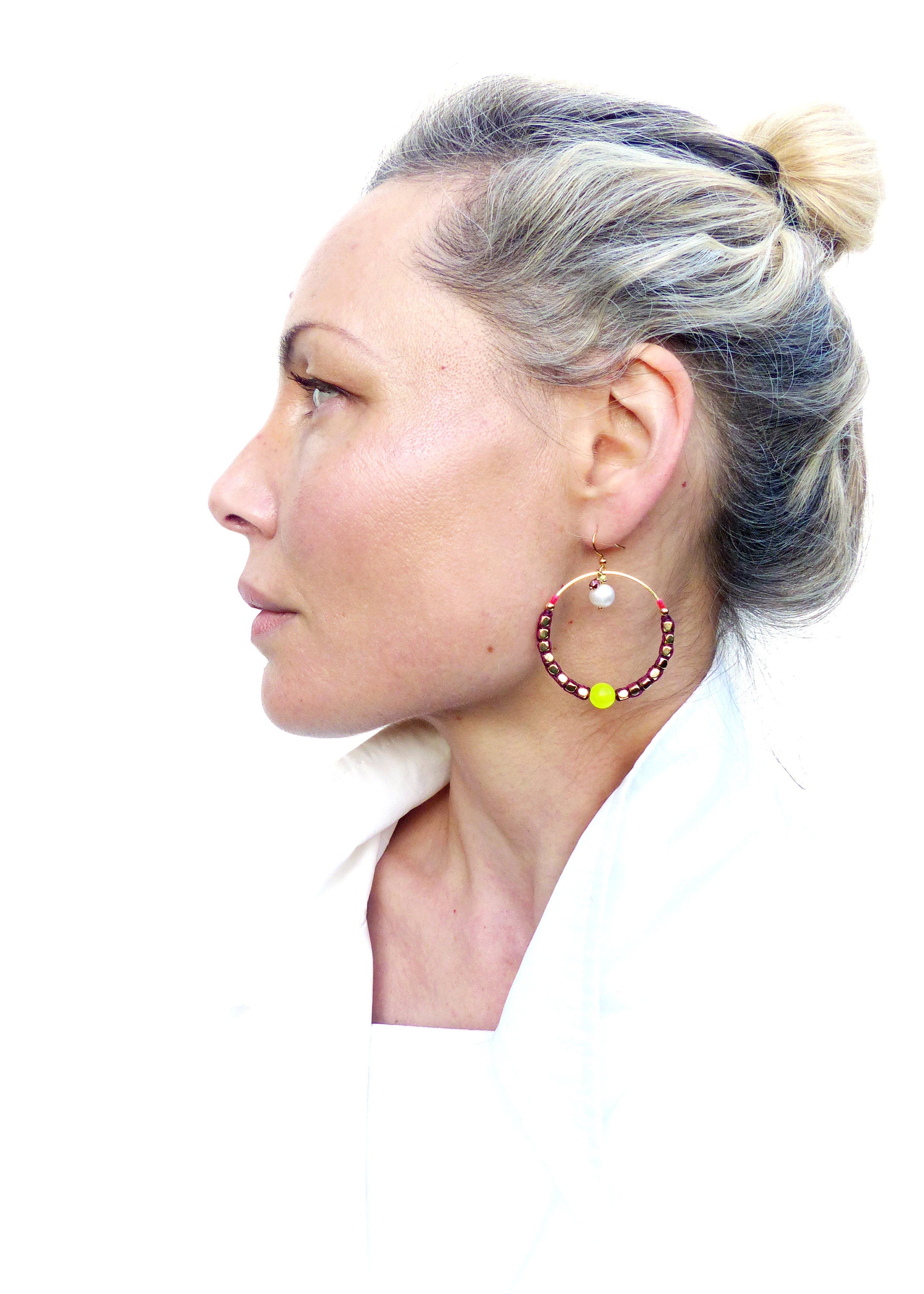 Peut inclure: Une femme portant une chemise blanche avec une paire de boucles d'oreilles créoles. Les boucles d'oreilles sont faites de perles brunes avec une seule perle blanche et une perle jaune vif.