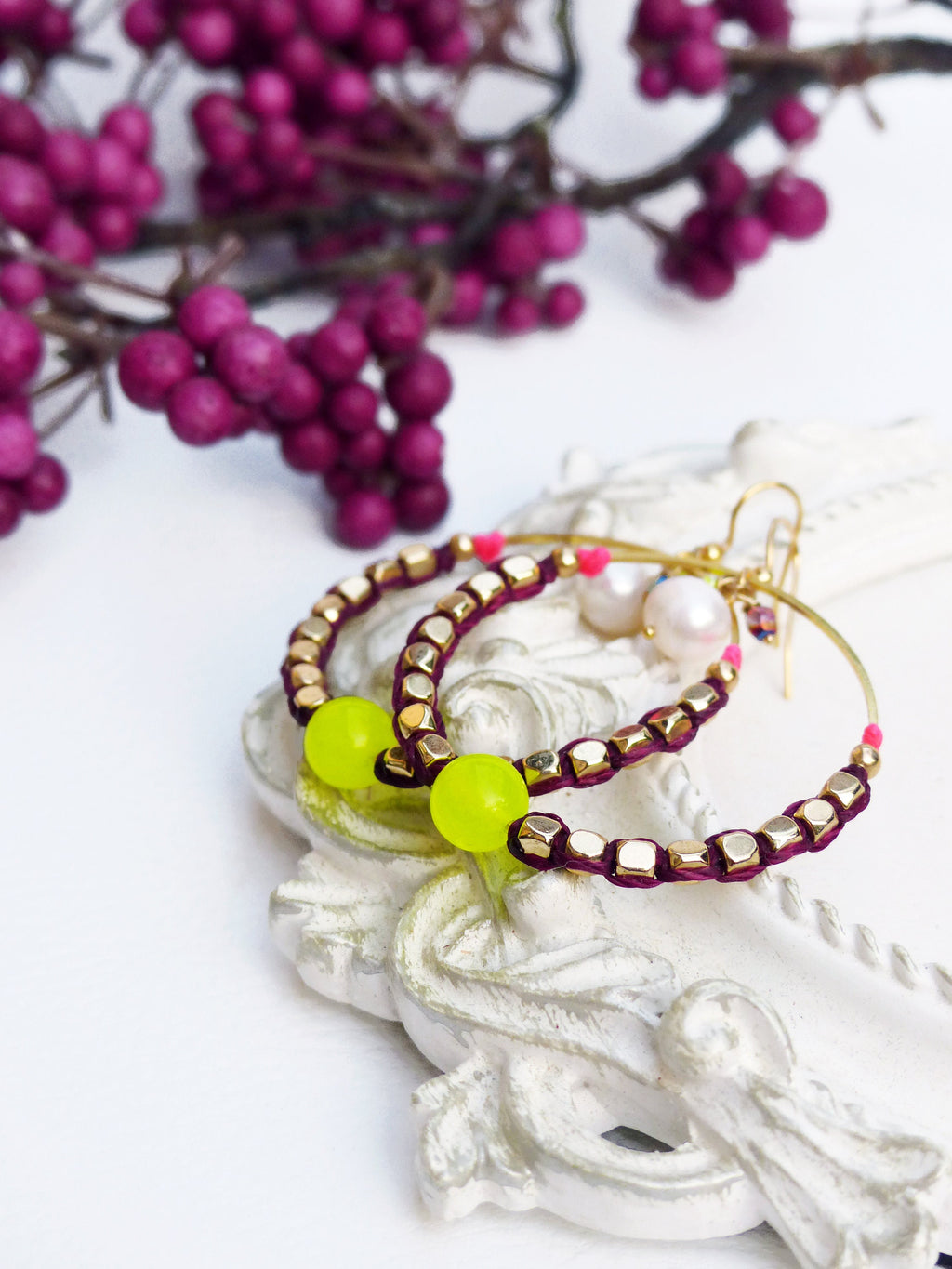 Peut inclure: Une paire de boucles d'oreilles créoles avec des perles dorées et un cordon bordeaux. Les boucles d'oreilles ont une perle jaune vif sur chaque créole.