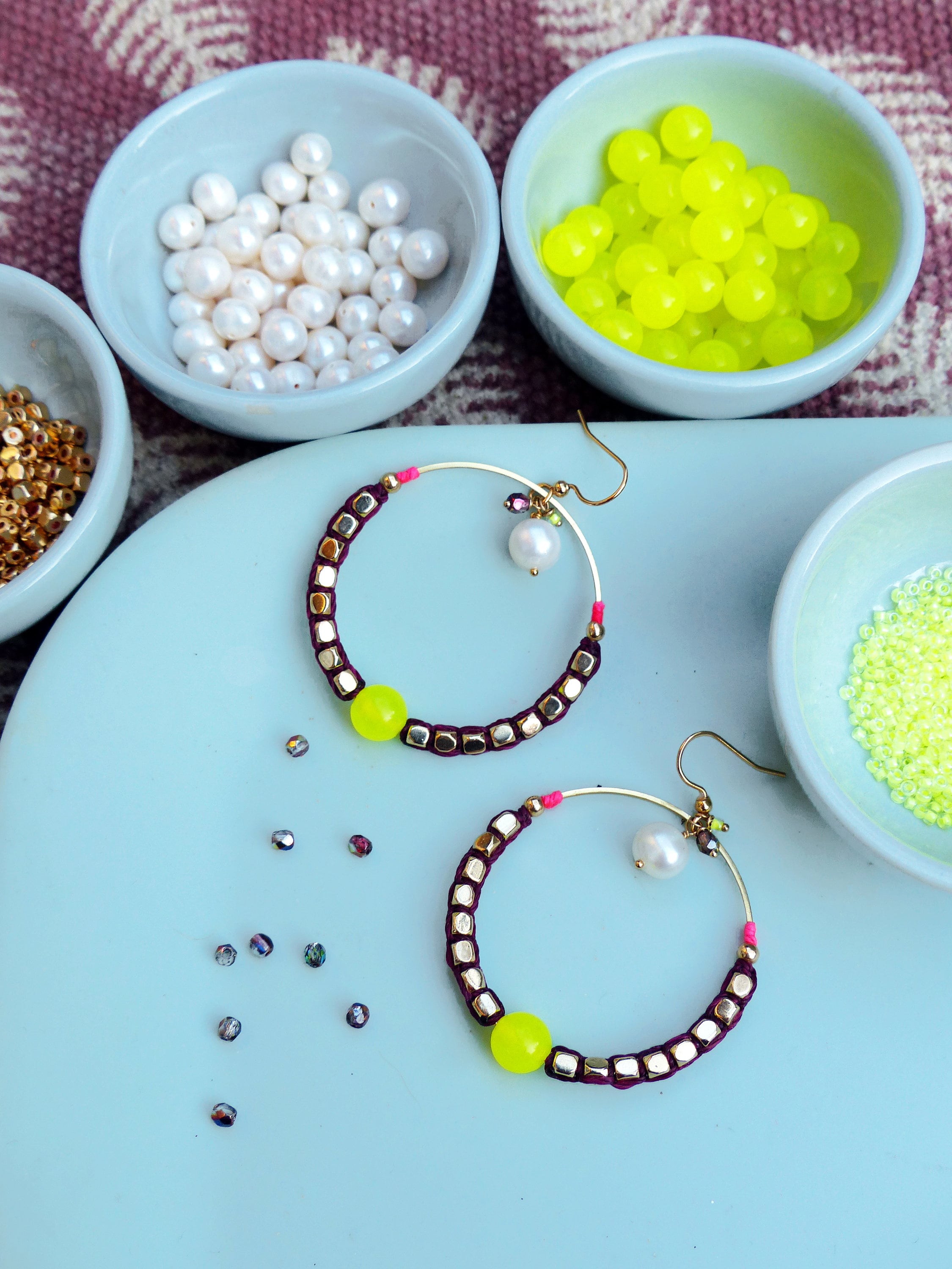 Peut inclure: Deux boucles d'oreilles créoles avec une base en fil d'or et un design de perles violettes et dorées. Chaque boucle d'oreille a une perle jaune vif et une perle blanche.