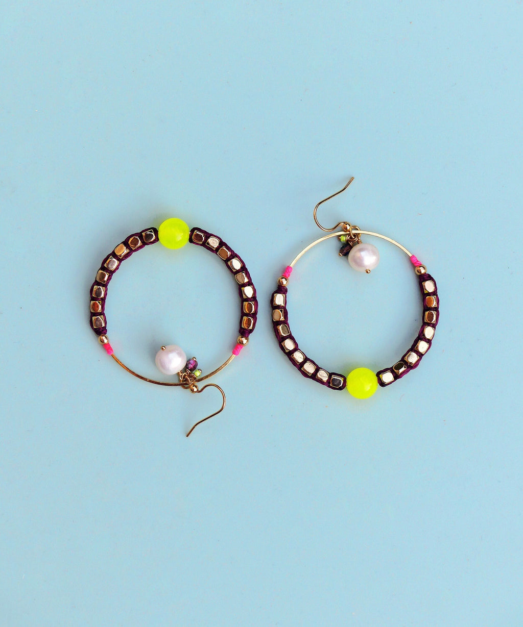 Peut inclure: Une paire de boucles d'oreilles créoles avec un cadre en fil d'or et des perles violettes et roses. Chaque boucle d'oreille a une perle jaune et une perle blanche.