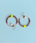 Peut inclure: Une paire de boucles d'oreilles créoles avec un cadre en fil d'or et des perles violettes et roses. Chaque boucle d'oreille a une perle jaune et une perle blanche.