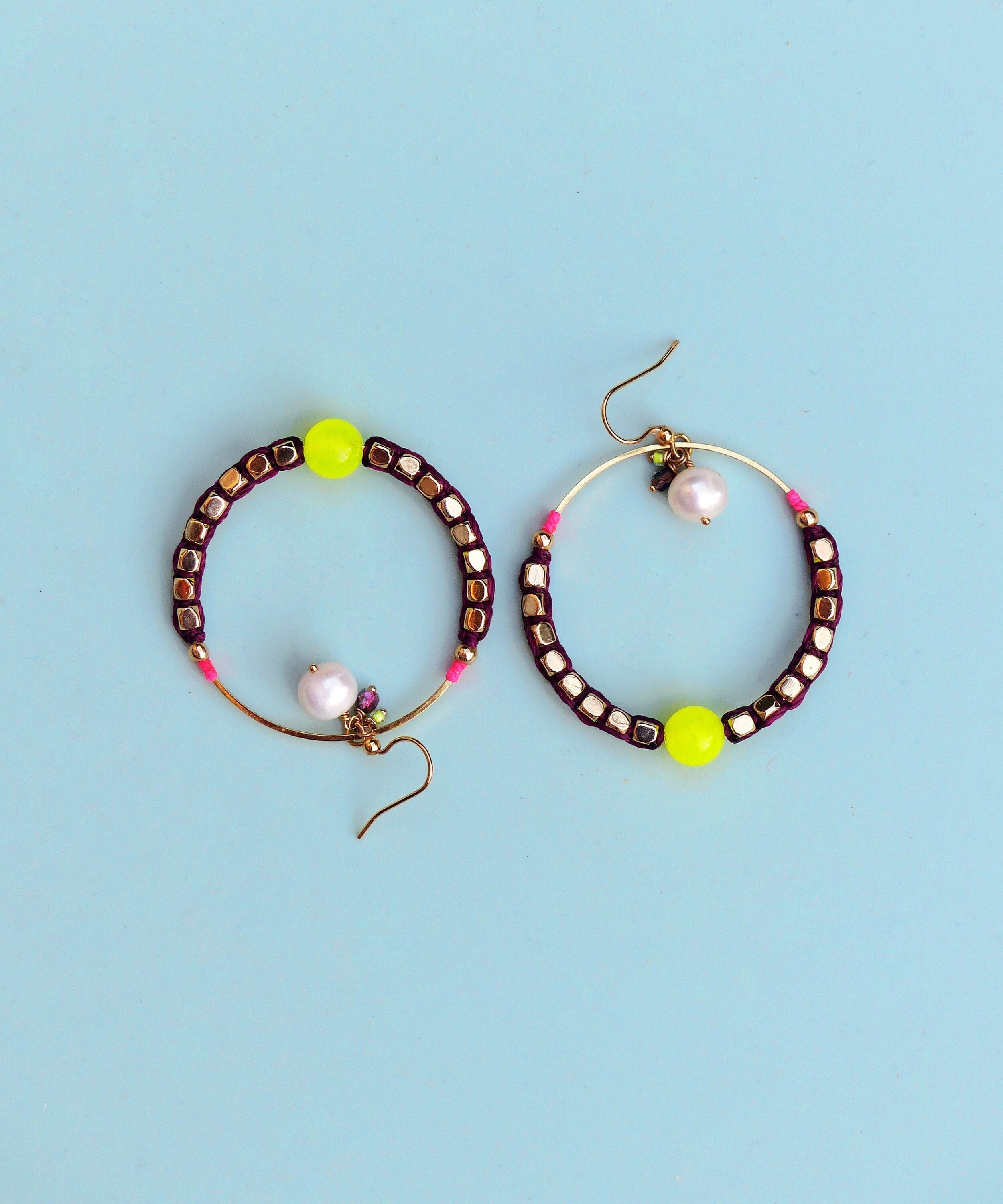 Peut inclure: Une paire de boucles d'oreilles créoles avec un cadre en fil d'or et des perles violettes et roses. Chaque boucle d'oreille a une perle jaune et une perle blanche.
