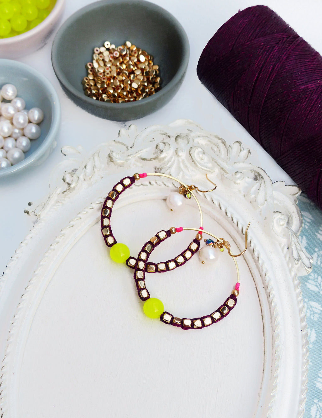 Peut inclure: Une paire de boucles d'oreilles créoles avec un cordon bordeaux et des perles dorées. Les boucles d'oreilles ont une perle jaune vif de chaque côté.