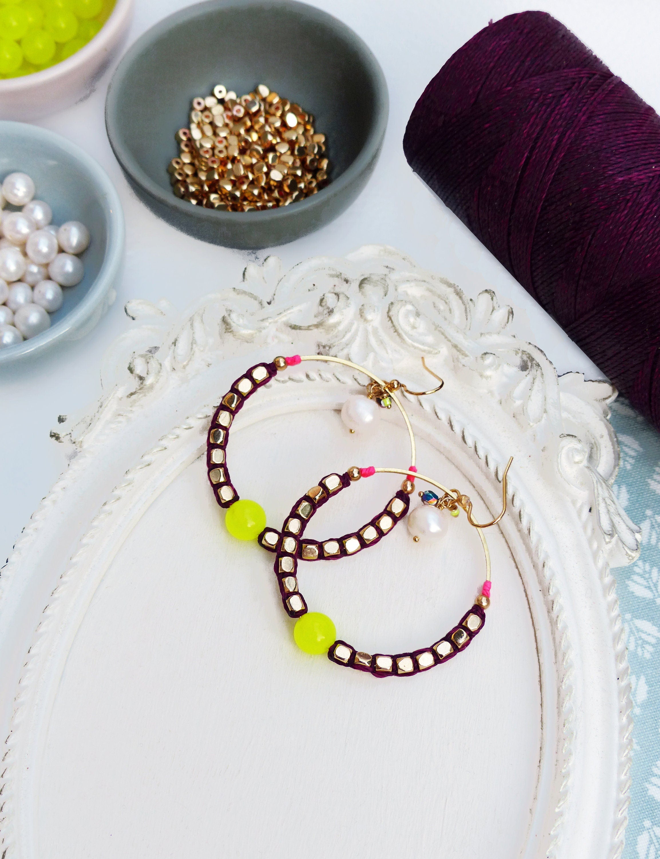 Peut inclure: Une paire de boucles d'oreilles créoles avec un cordon bordeaux et des perles dorées. Les boucles d'oreilles ont une perle jaune vif de chaque côté.