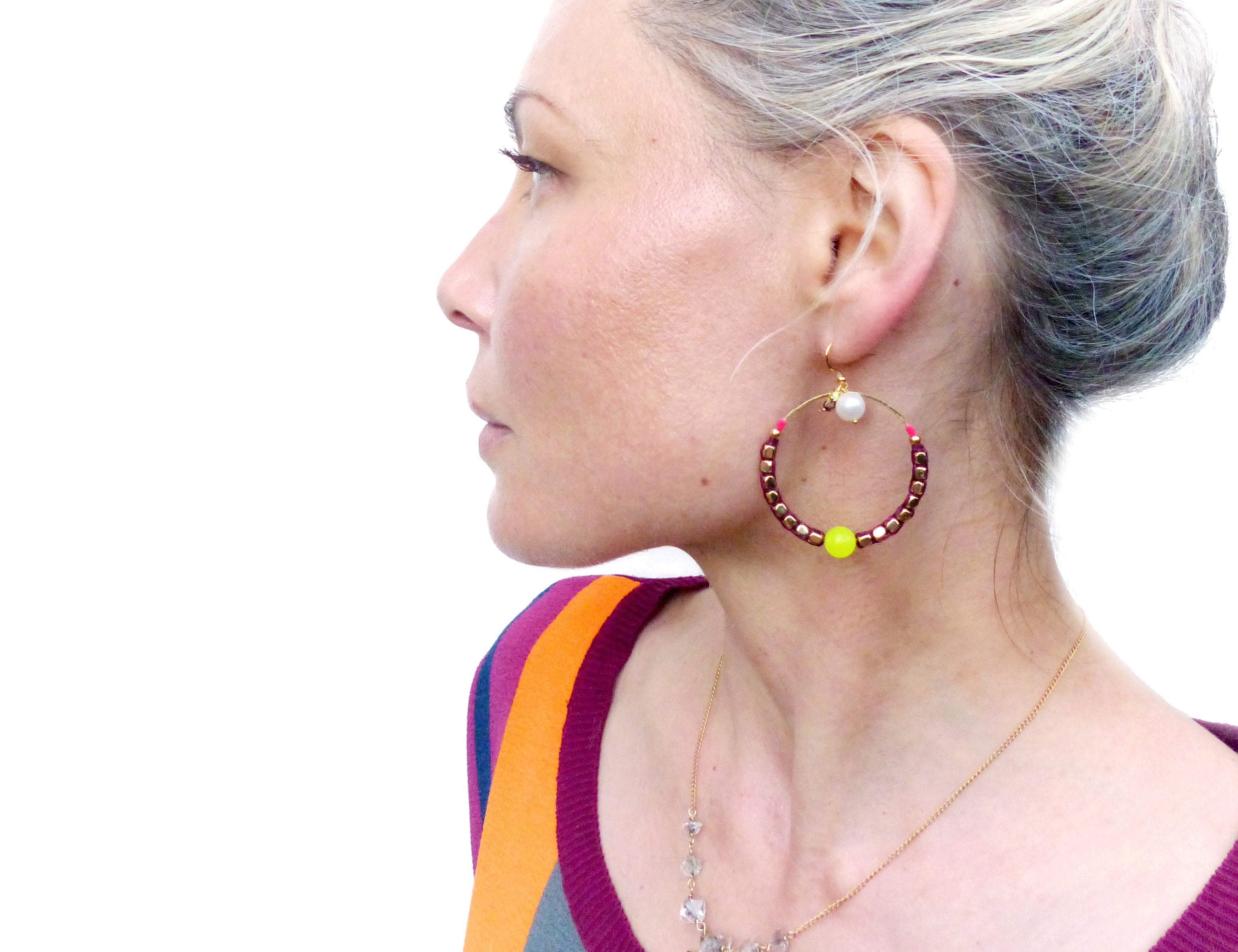 Peut inclure: Une paire de boucles d'oreilles créoles avec une base en fil d'or et des perles bordeaux. Une petite perle jaune et une perle blanche pendent du cercle.
