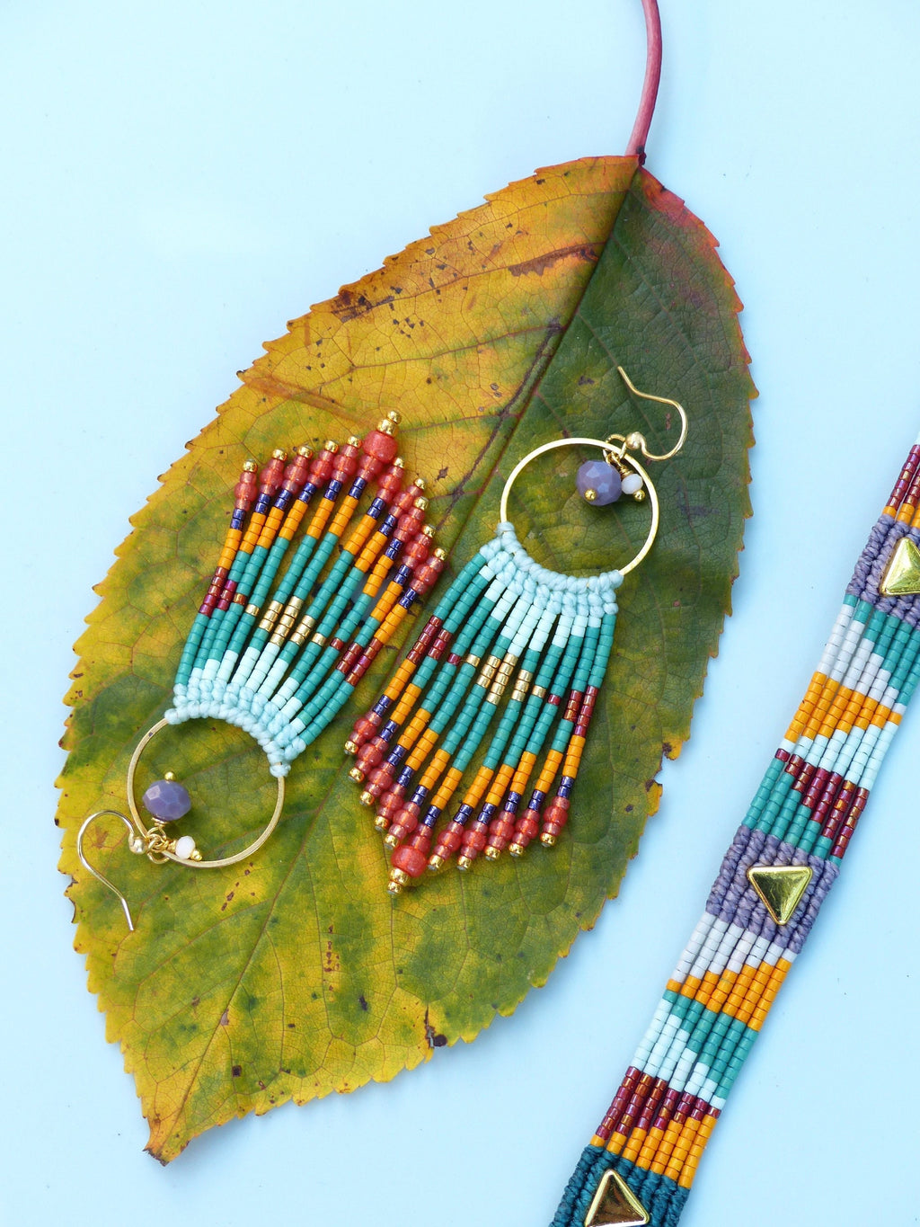 Peut inclure: Une paire de longues boucles d'oreilles en perles colorées avec des cercles dorés et un pendentif en pierre violette. Un bracelet en perles assorti avec des accents dorés est également présenté.