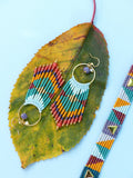 Peut inclure: Une paire de longues boucles d'oreilles en perles colorées avec des cercles dorés et un pendentif en pierre violette. Un bracelet en perles assorti avec des accents dorés est également présenté.