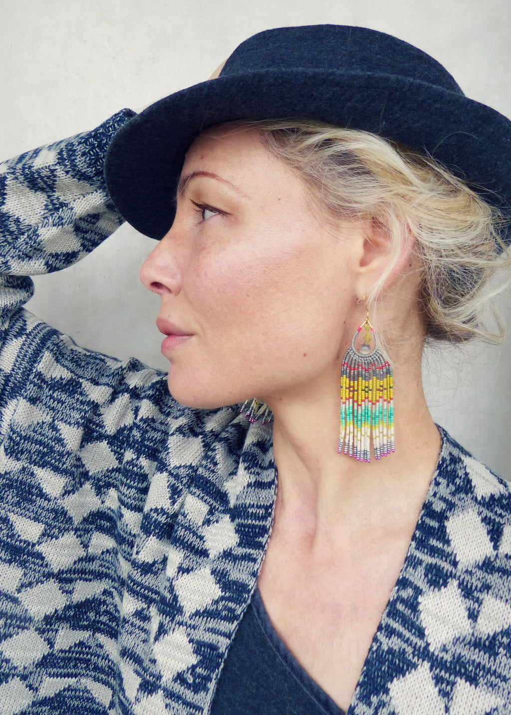 Peut inclure: Une femme portant un cardigan à motifs bleus et blancs avec un chapeau fedora noir. Elle porte de longues boucles d'oreilles en perles colorées.