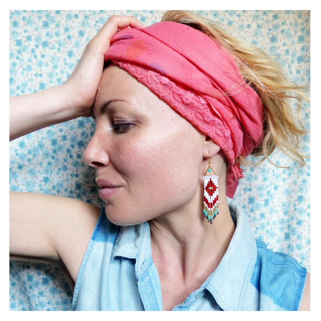 Peut inclure: Une femme portant un foulard rose avec une boucle d'oreille en perles blanches et rouges. La boucle d'oreille est un long design géométrique fin avec un motif rouge et blanc.