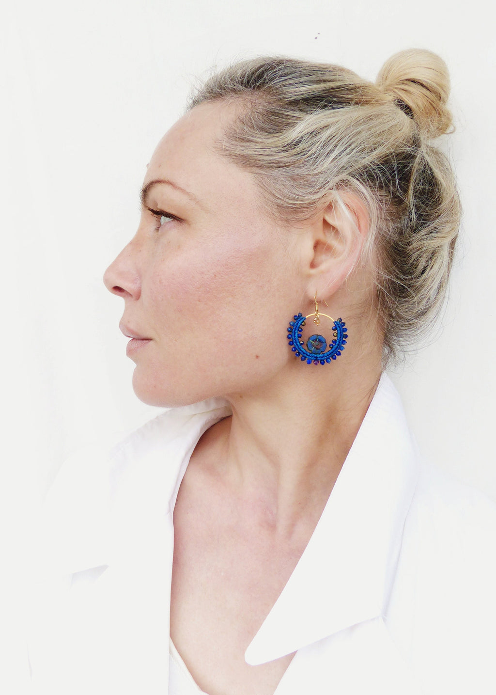 Peut inclure: Une femme portant une chemise blanche avec une boucle d'oreille en forme de cercle en perles bleues. La boucle d'oreille a un fil d'or et une pierre précieuse bleue au centre.