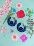 Peut inclure: Une paire de boucles d'oreilles créoles bleues avec une perle de verre bleue au centre de chaque créole. Les boucles d'oreilles sont entourées de fleurs séchées dans des tons de rose, bleu et blanc.