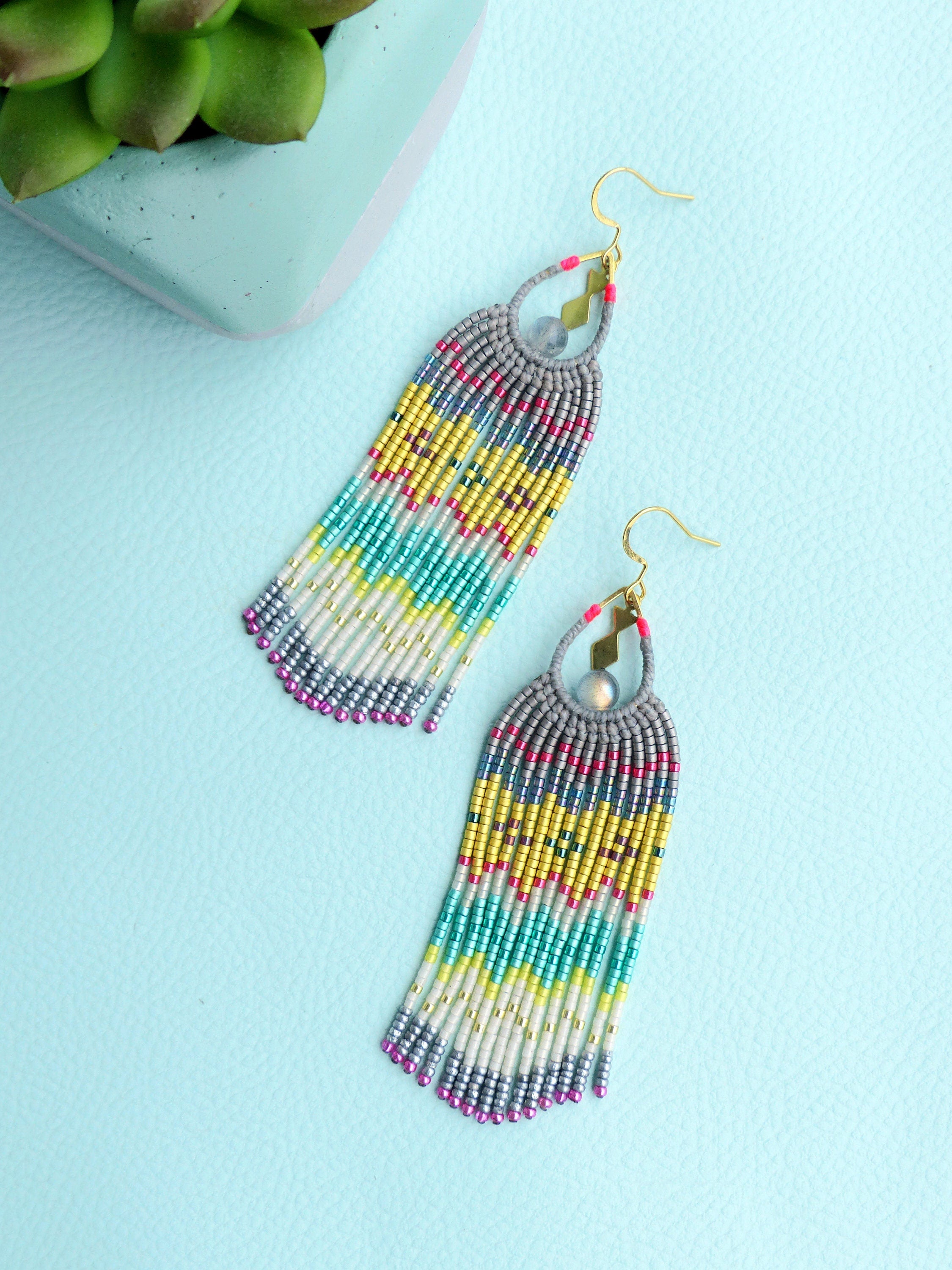 Peut inclure: Une paire de longues boucles d'oreilles à franges perlées avec un motif argenté, turquoise, jaune et rose. Les boucles d'oreilles ont un petit charme rond argenté en haut.