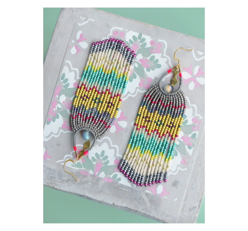 Peut inclure: Une paire de longues boucles d'oreilles en perles colorées avec un motif géométrique. Les boucles d'oreilles sont faites de perles argentées, dorées, blanches, turquoise et roses. Les boucles d'oreilles ont une fermeture à crochet dorée.