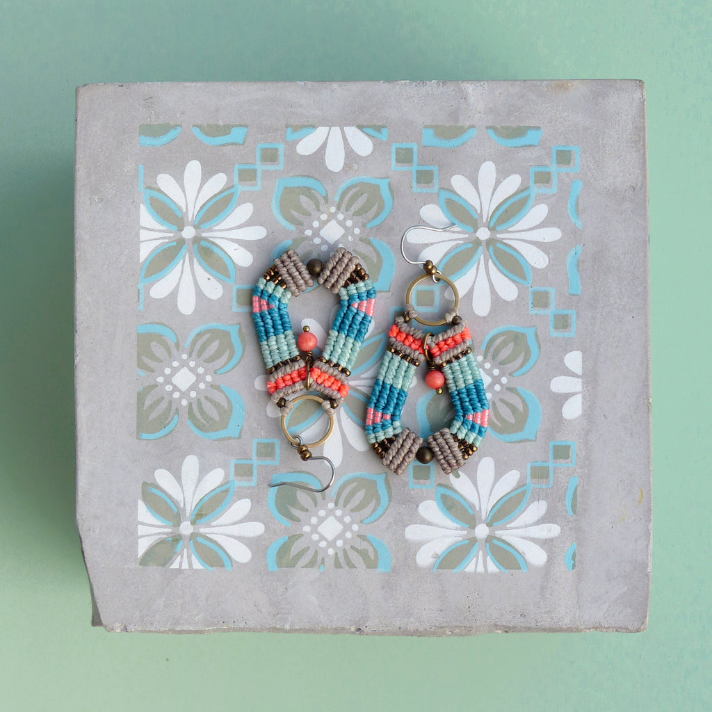 Peut inclure: Une paire de boucles d'oreilles faites à la main avec un design géométrique. Les boucles d'oreilles sont faites avec des perles brunes, bleues, roses et orange. Les boucles d'oreilles sont suspendues à des anneaux dorés.