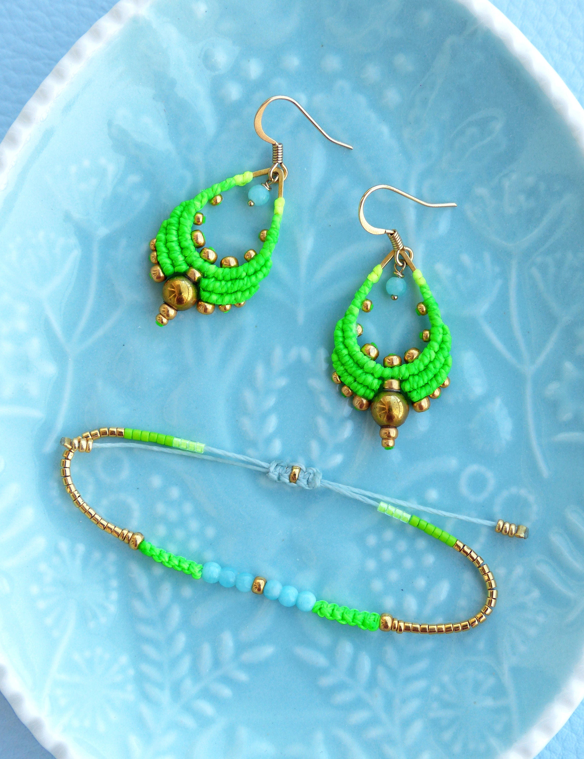 Peut inclure: Un ensemble de boucles d'oreilles et d'un bracelet assorti en perles vertes et bleues. Les boucles d'oreilles sont en forme de goutte et ont un accent doré. Le bracelet est fait de petites perles et a un fermoir doré.