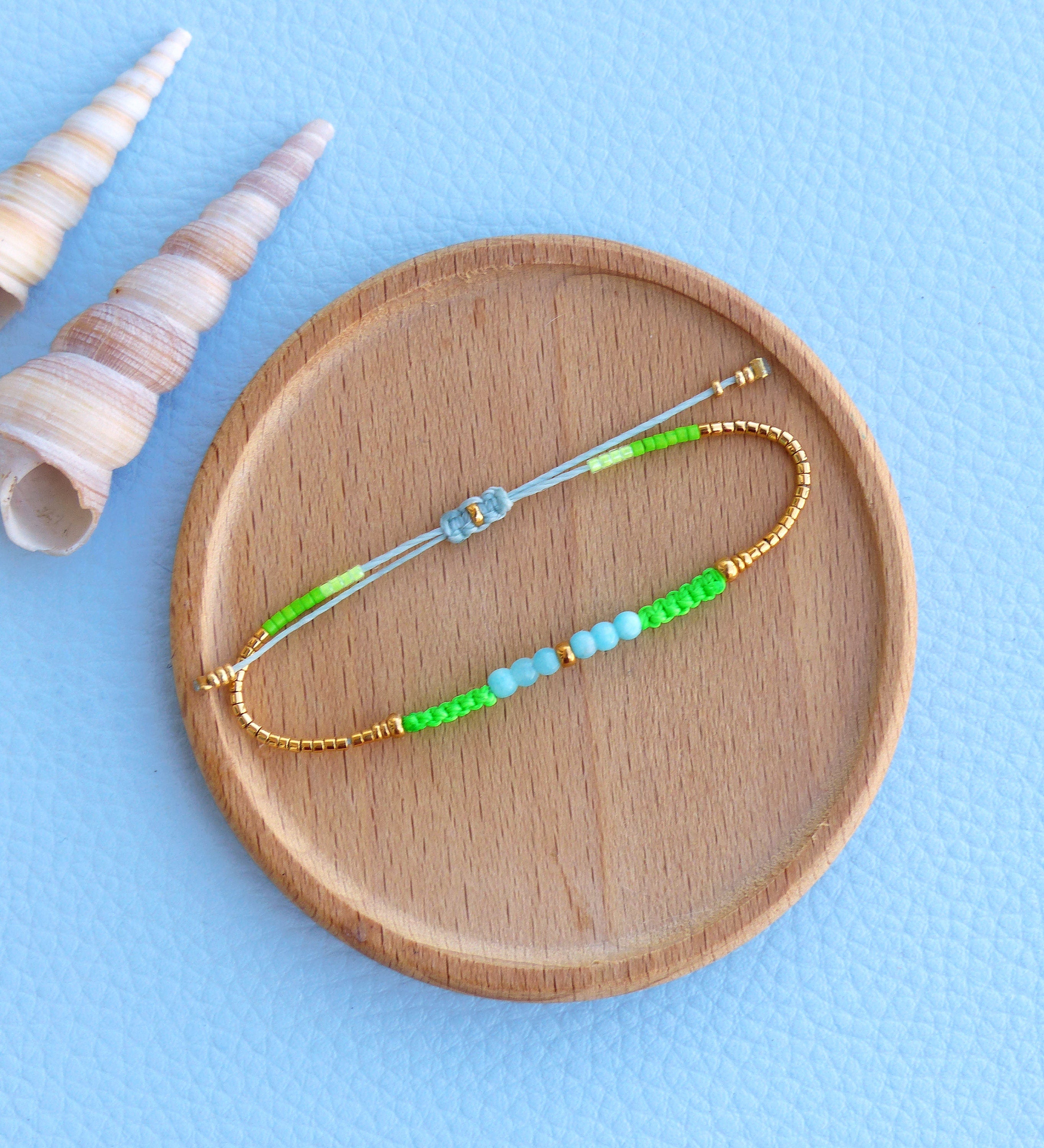 Peut inclure: Un bracelet délicat composé de petites perles vertes et bleues, enfilées sur un fil doré. Le bracelet est noué avec un cordon blanc et vert.