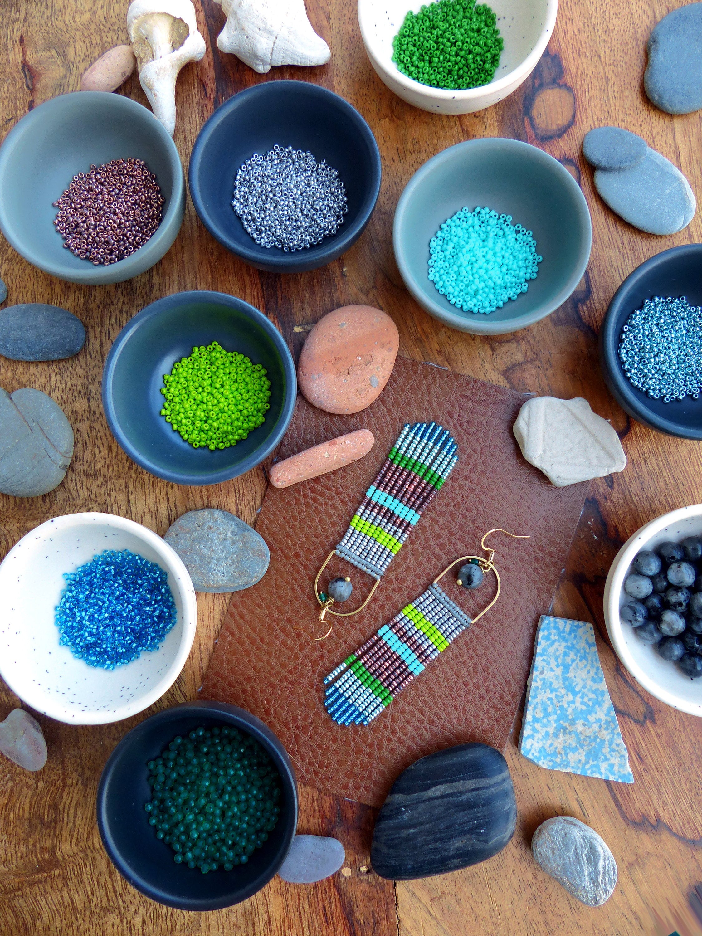 Peut inclure: Une paire de boucles d'oreilles en perles faites à la main avec un motif géométrique. Les boucles d'oreilles sont faites avec une variété de couleurs, notamment le vert, le bleu, le marron et le gris. Les boucles d'oreilles sont suspendues à des crochets dorés.