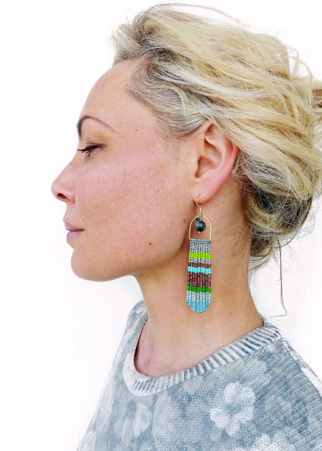 Peut inclure: Une paire de longues boucles d'oreilles en perles avec un anneau en or et une perle bleu foncé au sommet. Les perles sont disposées en un motif rayé de bleu, vert, marron et argent.