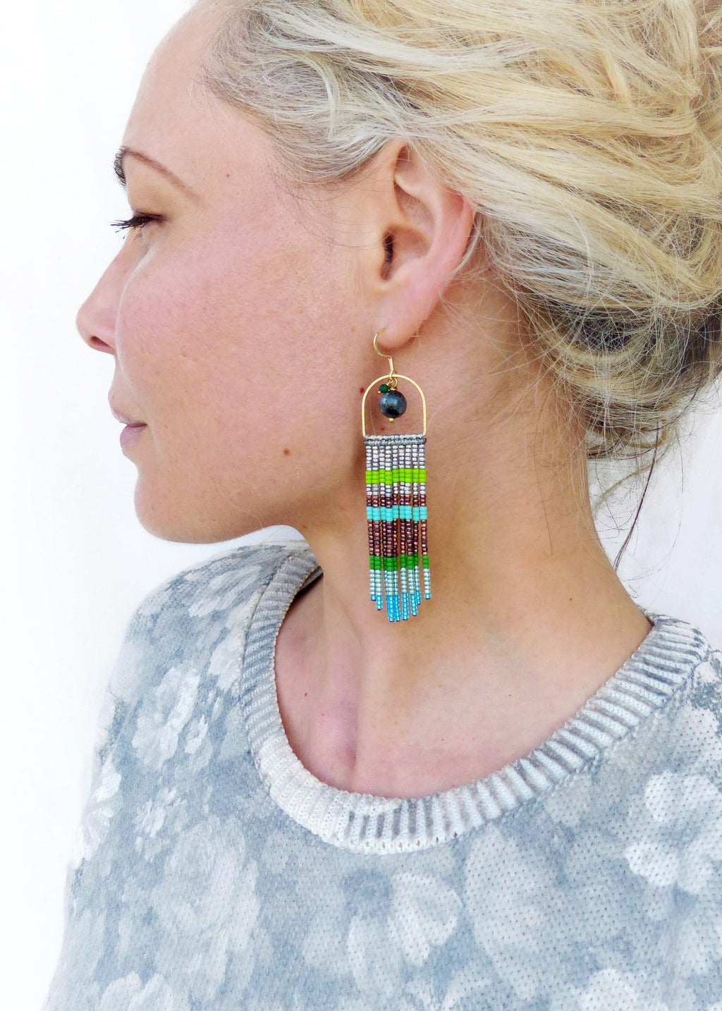 Peut inclure: Une paire de longues boucles d'oreilles en perles avec une arche dorée et une perle gris foncé. Les boucles d'oreilles présentent un mélange de perles vertes, bleues, argentées et brunes.