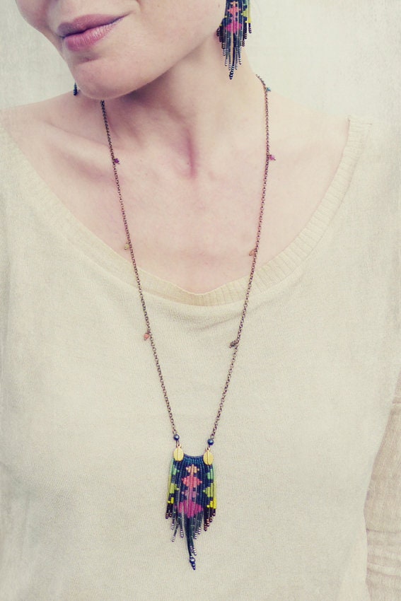 Peut inclure: Un long collier de perles avec un pendentif géométrique coloré pend au cou d'une femme. Le pendentif est fait de petites perles colorées et a un design en forme de frange. Le collier est fait d'une fine chaîne argentée.