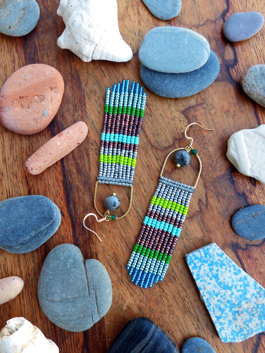 Peut inclure: Une paire de longues boucles d'oreilles en perles avec un schéma de couleurs argent, vert, bleu et marron. Les boucles d'oreilles sont suspendues à des crochets dorés.