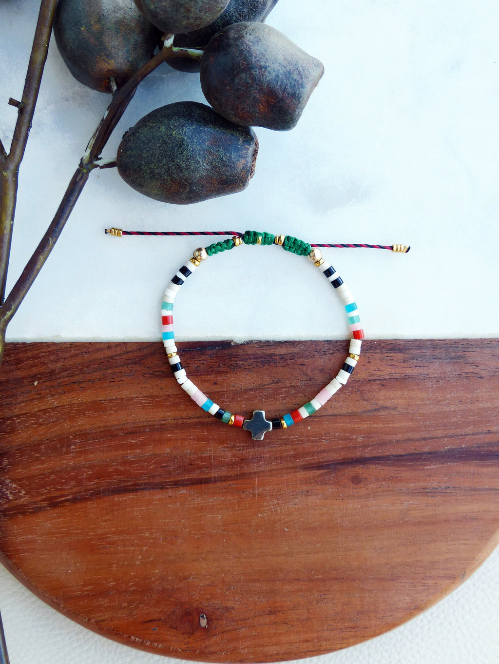 Peut inclure: Un bracelet coloré en perles avec un pendentif en forme de croix argentée. Le bracelet est composé de petites perles rondes dans des tons de blanc, noir, rouge, bleu et vert. Les perles sont enfilées sur un cordon fin rouge avec des accents dorés.