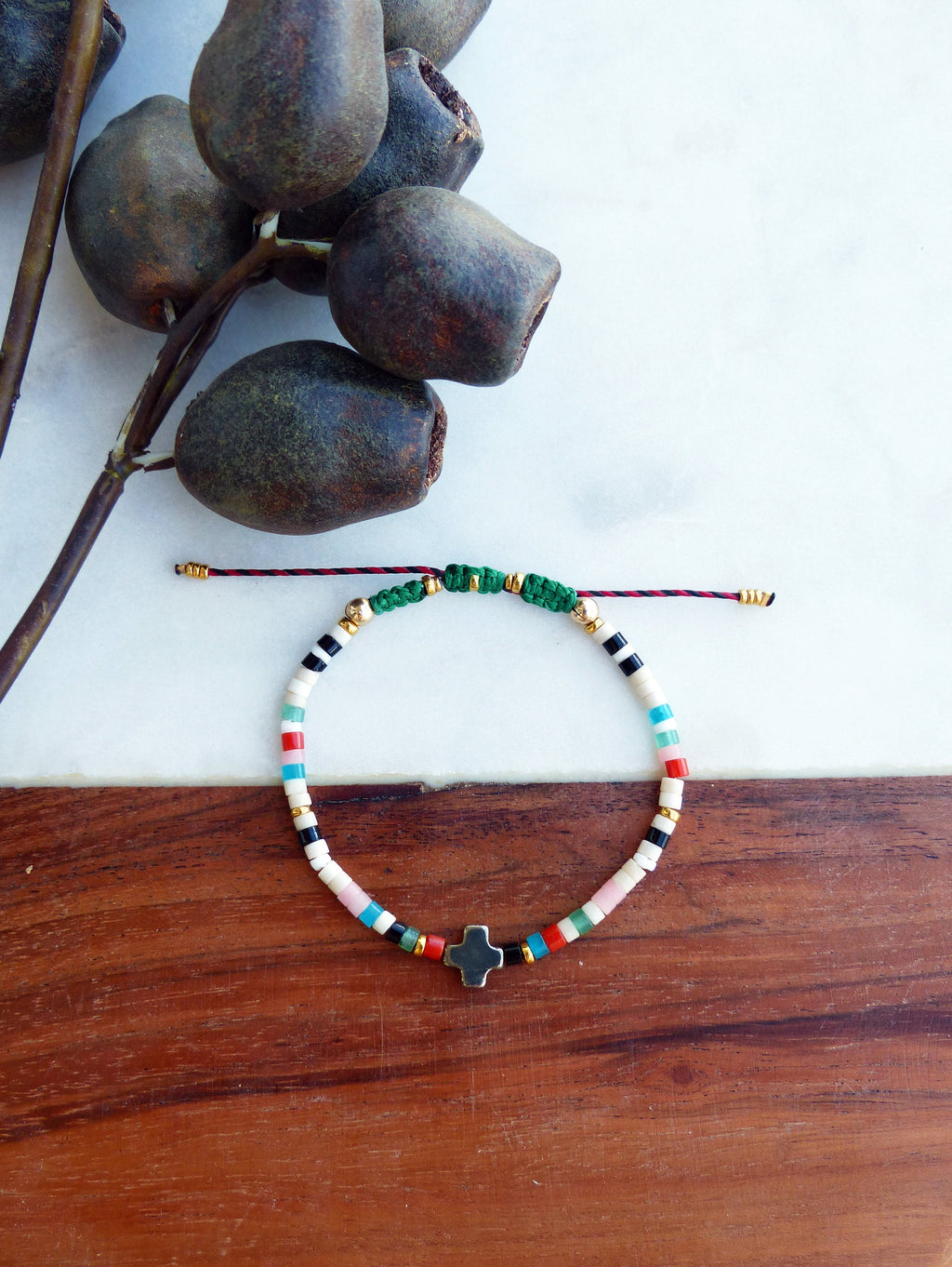 Peut inclure: Un bracelet coloré en perles avec un petit charme en forme de croix. Le bracelet est fait de perles blanches, noires, roses, bleues, vertes et rouges. Le charme en forme de croix est en métal foncé.