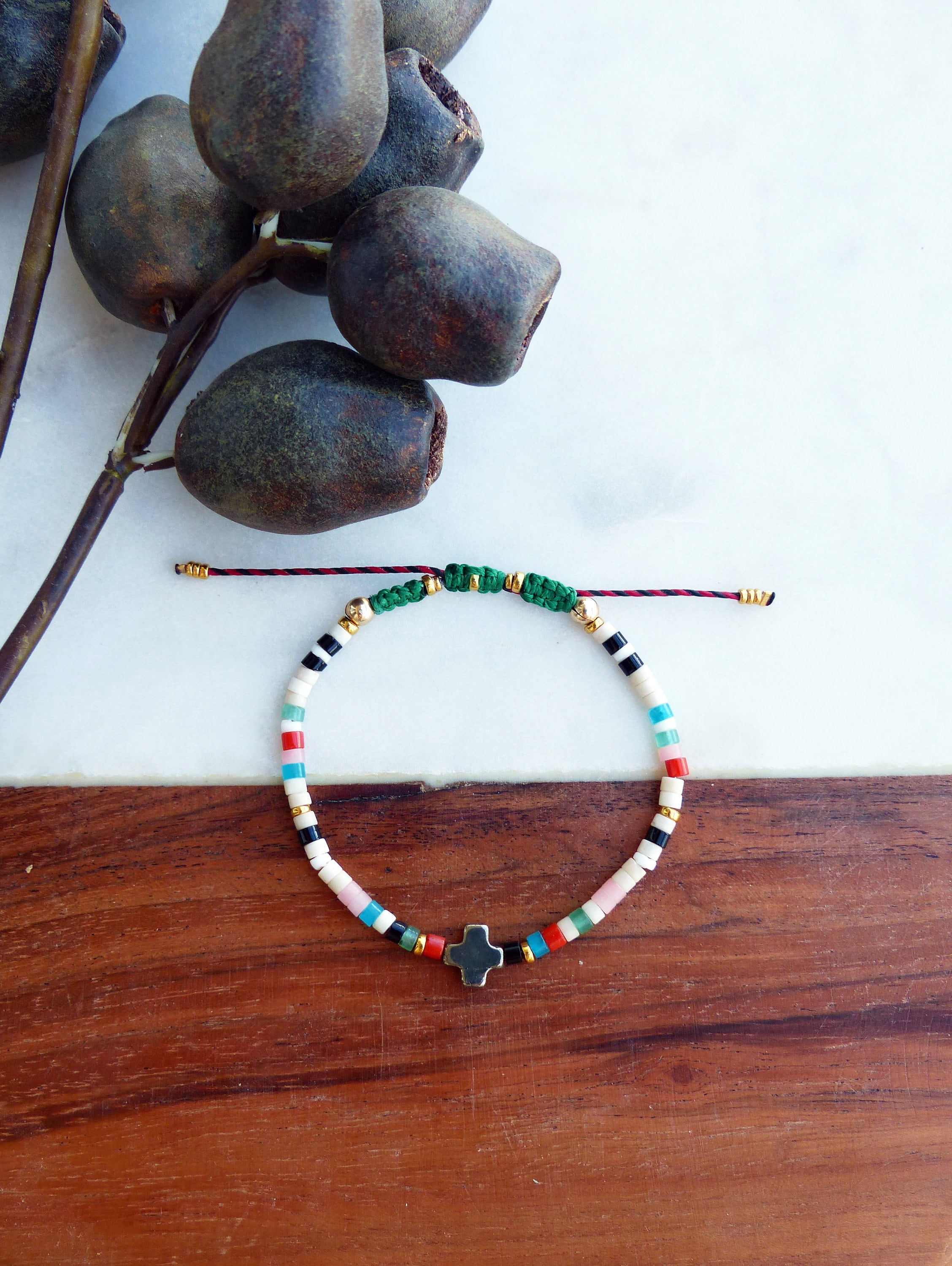 Peut inclure: Un bracelet coloré en perles avec un petit charme en forme de croix. Le bracelet est fait de perles blanches, noires, roses, bleues, vertes et rouges. Le charme en forme de croix est en métal foncé.