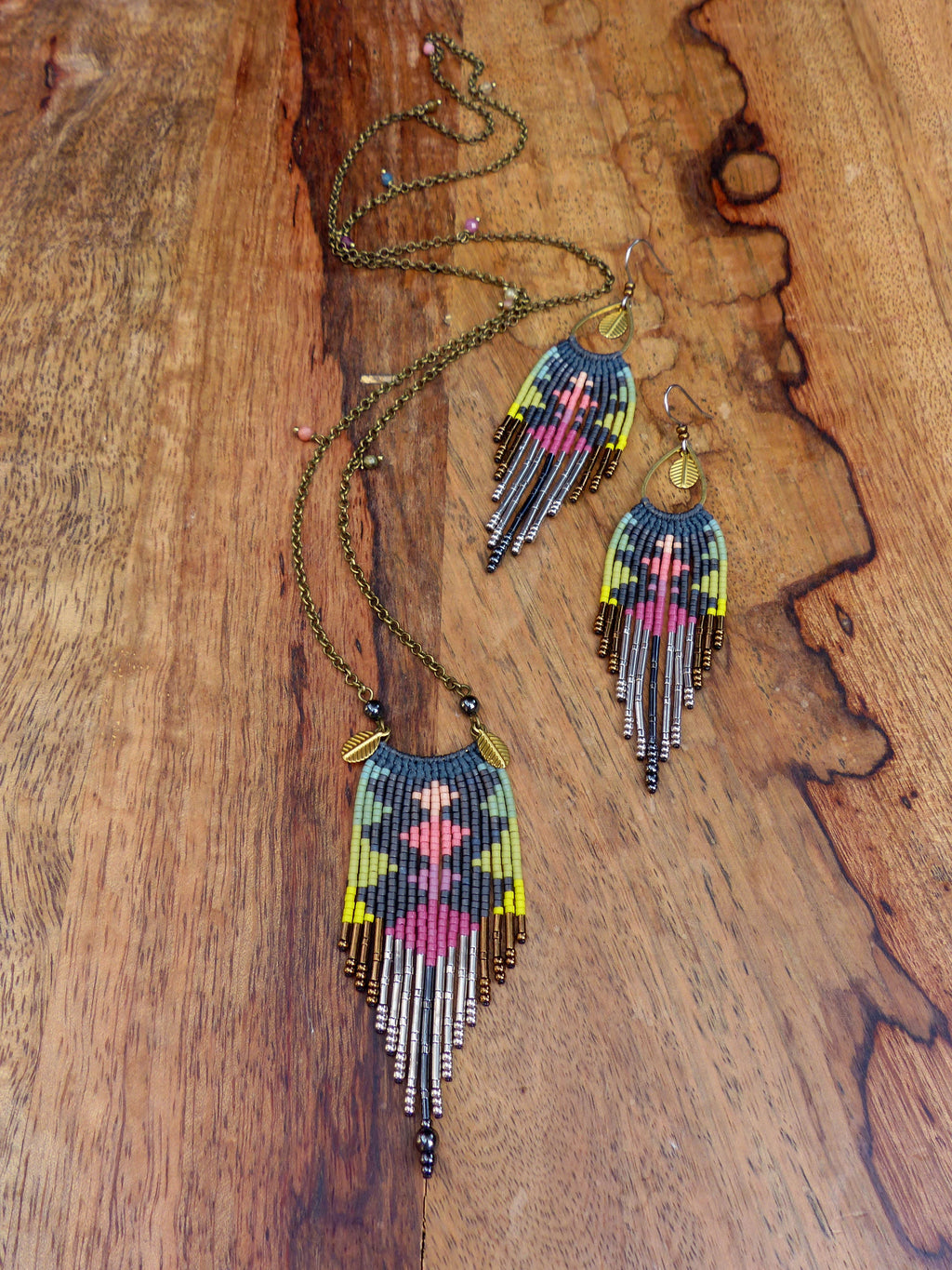 Peut inclure: Un ensemble de bijoux en perles comprenant un long collier et des boucles d'oreilles assorties. Le collier et les boucles d'oreilles présentent un motif géométrique dans des tons de rose, vert, jaune et noir. Les bijoux sont faits de petites perles et ont un design en forme de frange.