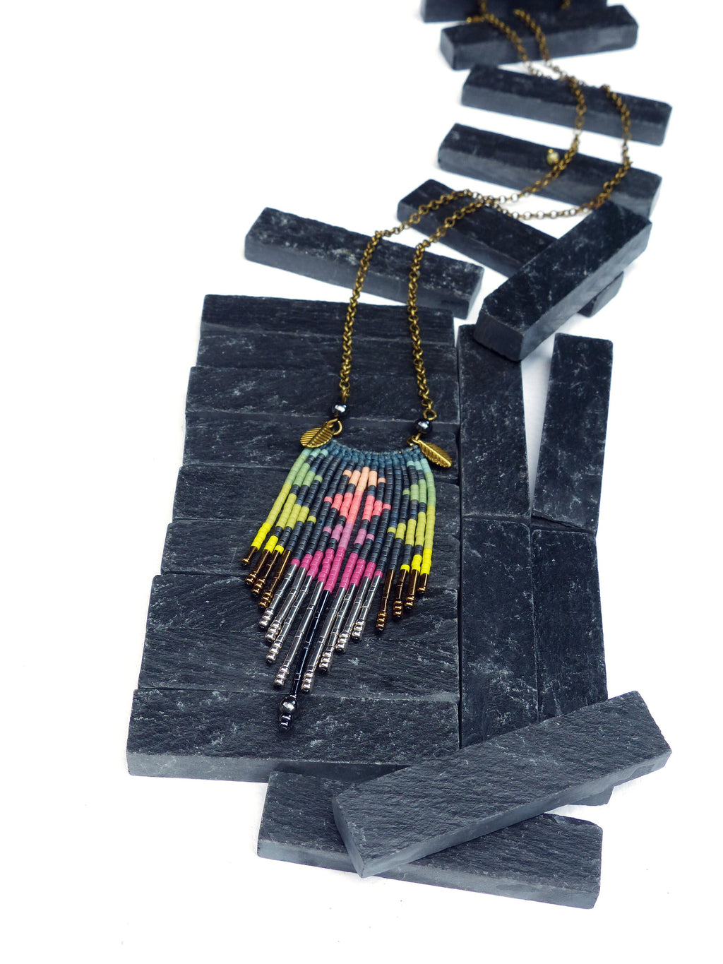 Peut inclure: Un collier de perles coloré avec un motif géométrique pend d'une chaîne dorée sur un fond de schiste noir.