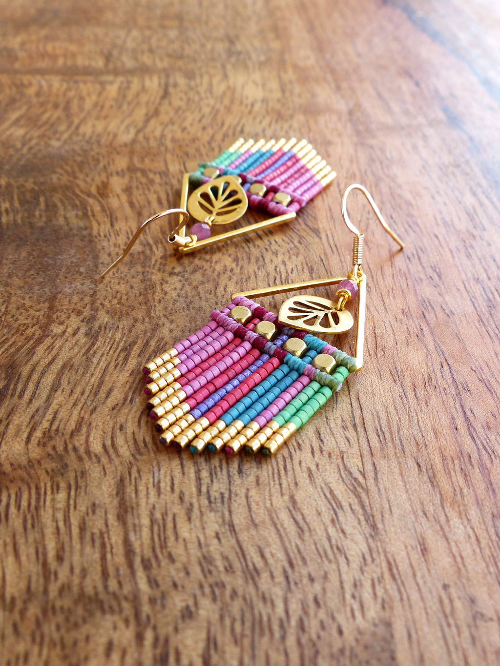 Peut inclure: Une paire de boucles d'oreilles en perles colorées avec des accents dorés et un charme en forme de feuille. Les boucles d'oreilles sont faites de petites perles colorées et ont une forme géométrique.