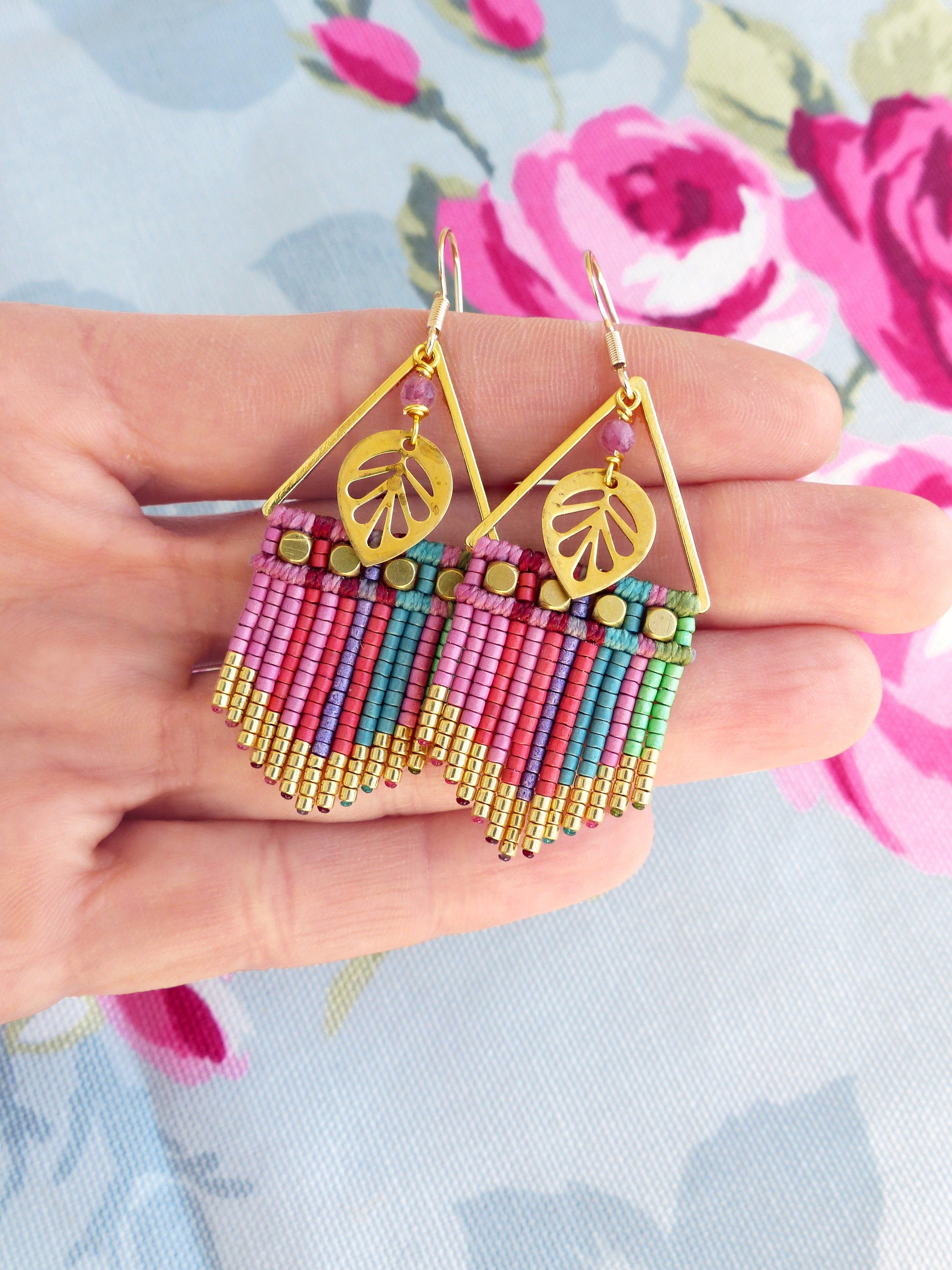 Peut inclure: Une paire de boucles d'oreilles pendantes triangulaires dorées avec des franges de perles roses, vertes et bleues et un charme en forme de feuille dorée.