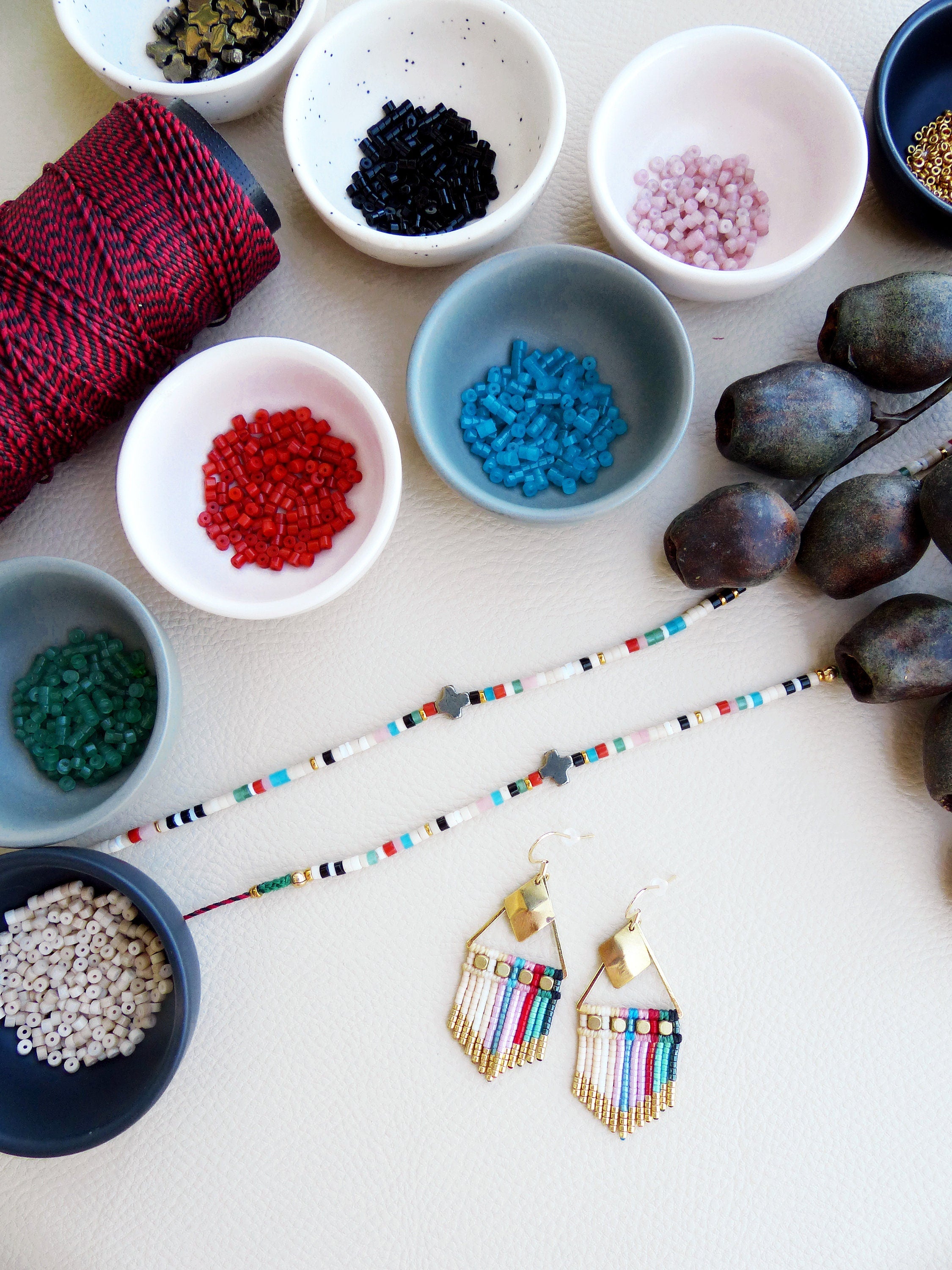 Peut inclure: Un collier de perles blanches et multicolores avec deux boucles d'oreilles en or et perles multicolores. Le collier et les boucles d'oreilles sont disposés sur une surface blanche avec de petits bols de perles de différentes couleurs.