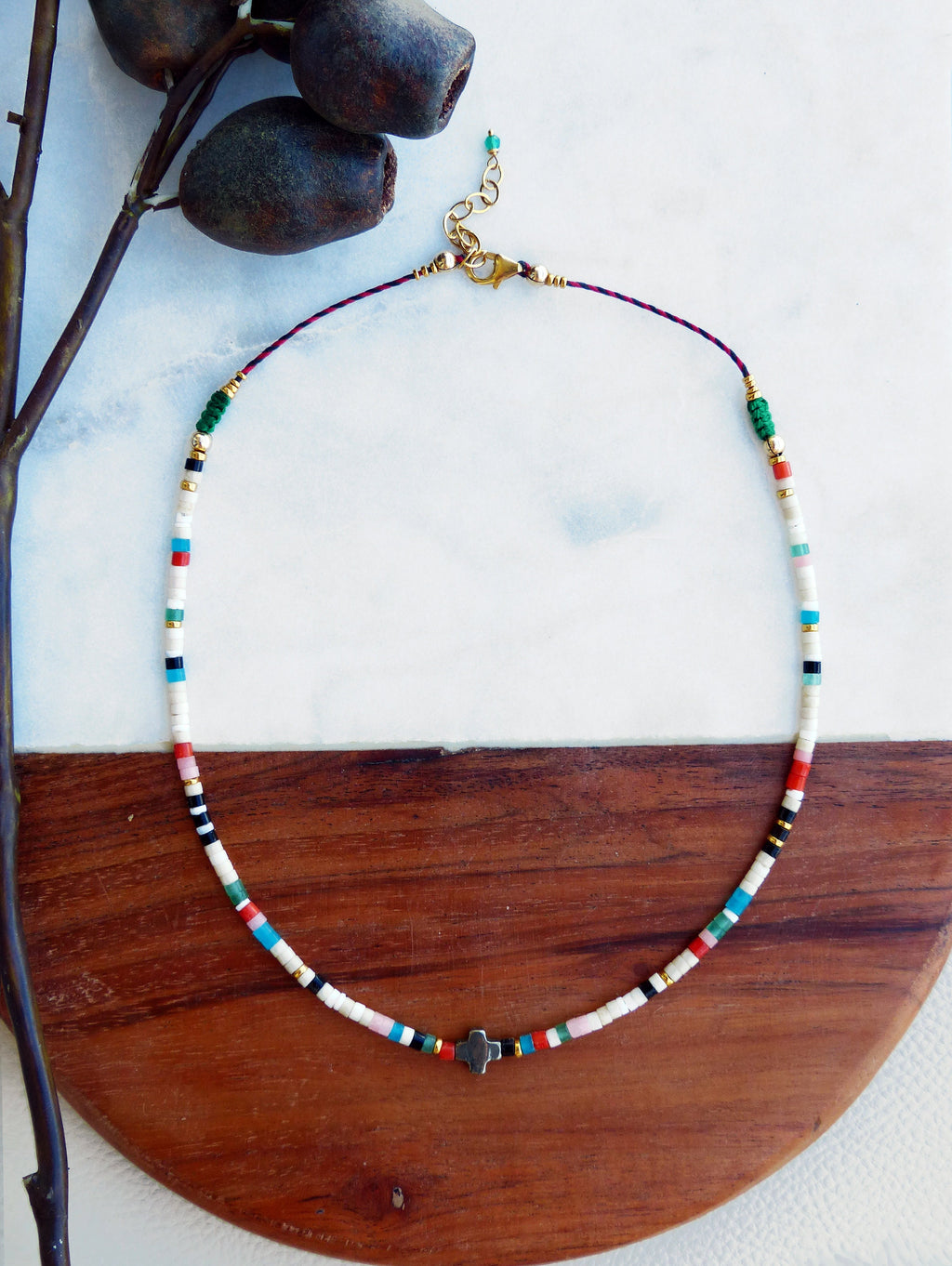 Peut inclure: Un collier de perles colorées avec un petit pendentif en forme de croix. Le collier est composé de perles blanches, noires, rouges, bleues, vertes et roses. Les perles sont enfilées sur un cordon fin.