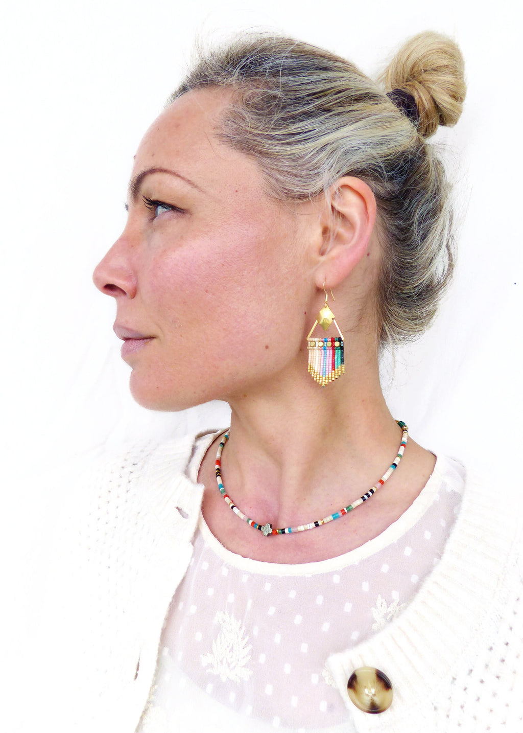 Peut inclure: Une femme portant un cardigan blanc et un haut blanc à petits pois noirs. Elle porte un collier de perles colorées et des boucles d'oreilles assorties.