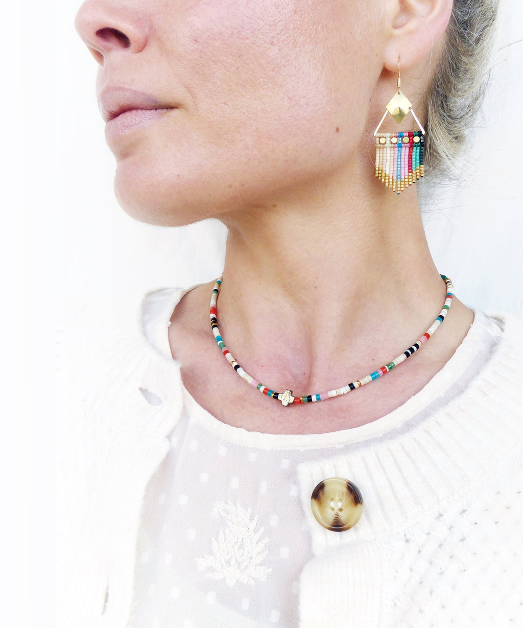 Peut inclure: Un collier de perles colorées avec un pendentif en or. Le collier est composé de petites perles rondes de différentes couleurs, notamment blanc, rouge, bleu, vert et noir. Le pendentif est une petite croix dorée.