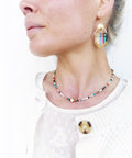 Peut inclure: Un collier de perles colorées avec un pendentif en or. Le collier est composé de petites perles rondes de différentes couleurs, notamment blanc, rouge, bleu, vert et noir. Le pendentif est une petite croix dorée.
