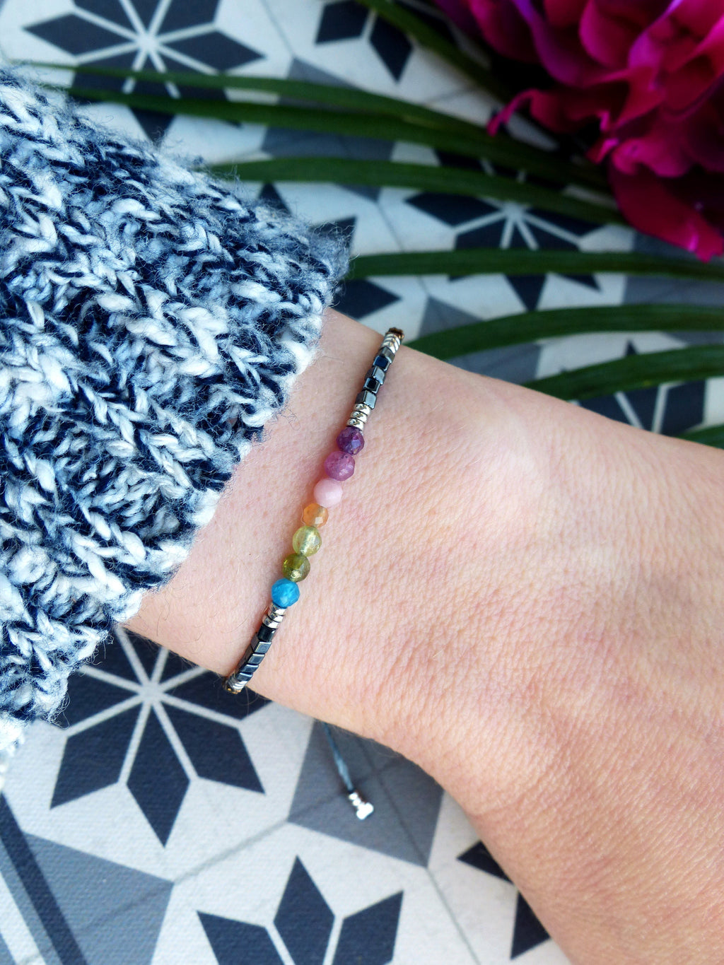 Peut inclure: Un bracelet en pierres précieuses arc-en-ciel avec un fermoir argenté et un cordon noir. Le bracelet présente une variété de pierres précieuses colorées, notamment turquoise, vert, jaune, orange, rose et violet.