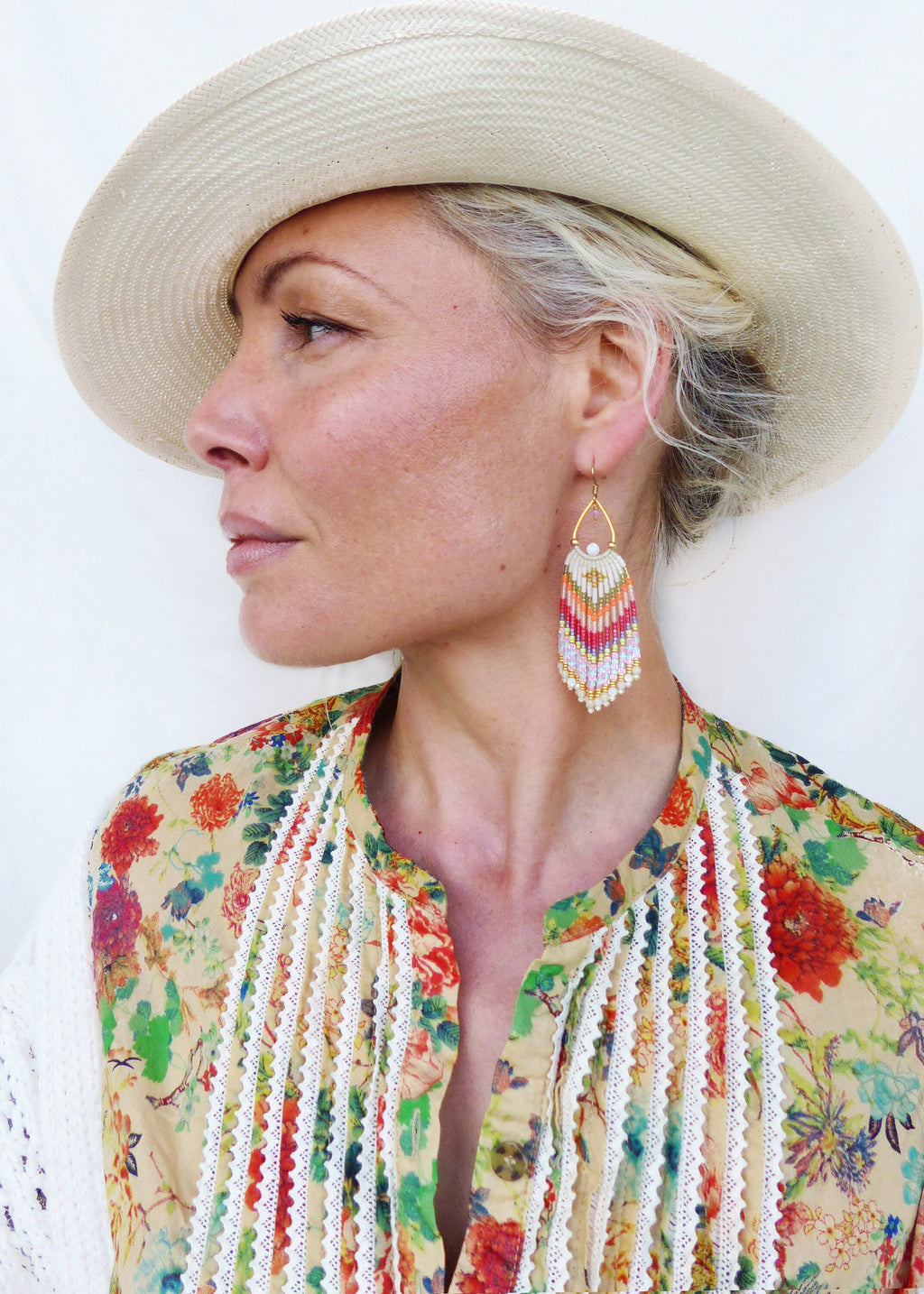 Peut inclure: Une femme portant un chapeau de paille et une blouse à imprimé floral avec des bordures en dentelle blanche. Elle porte de longues boucles d'oreilles en perles colorées.