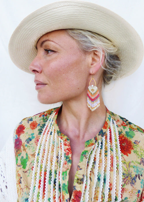 Peut inclure: Une femme portant un chapeau de paille et une blouse à imprimé floral avec des bordures en dentelle blanche. Elle porte de longues boucles d'oreilles en perles colorées.