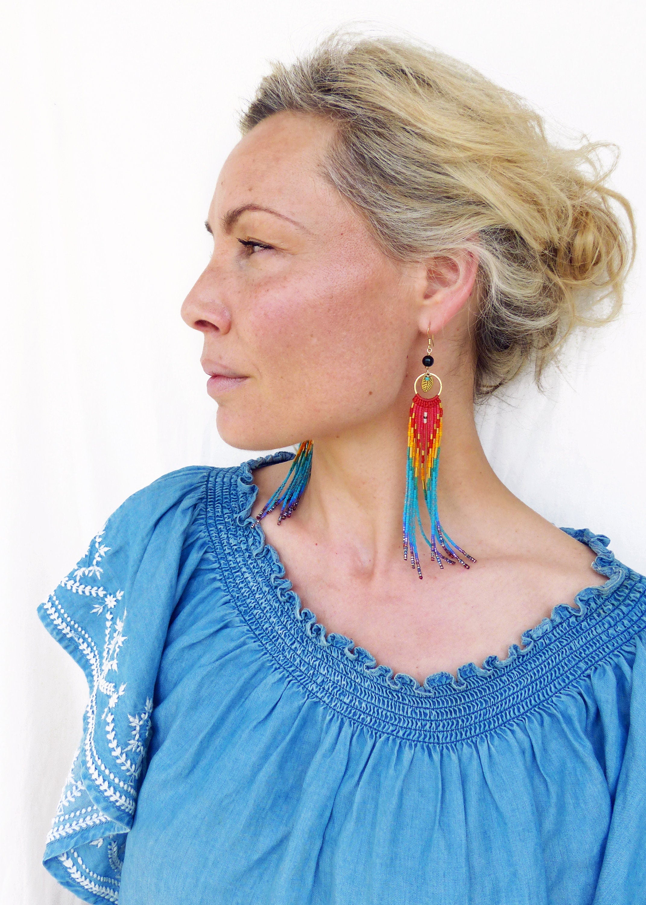 Peut inclure: Une femme portant un haut bleu denim à épaules dénudées avec des broderies blanches et de longues boucles d'oreilles en perles avec un dégradé de couleurs arc-en-ciel.