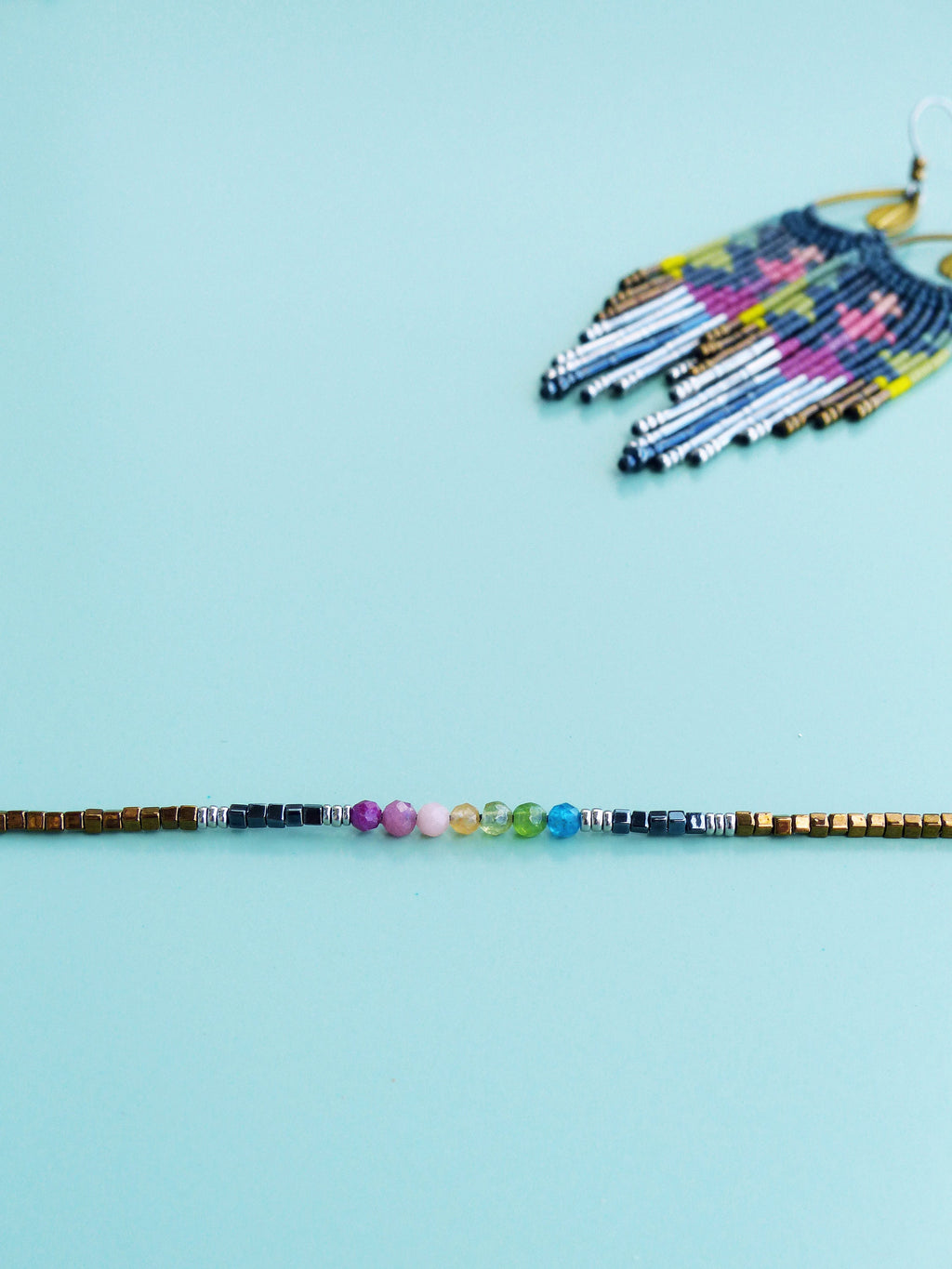 Peut inclure: Un bracelet en pierres précieuses arc-en-ciel avec des perles dorées et argentées. Le bracelet présente une variété de pierres précieuses colorées, notamment du rose, du jaune, du vert et du bleu.
