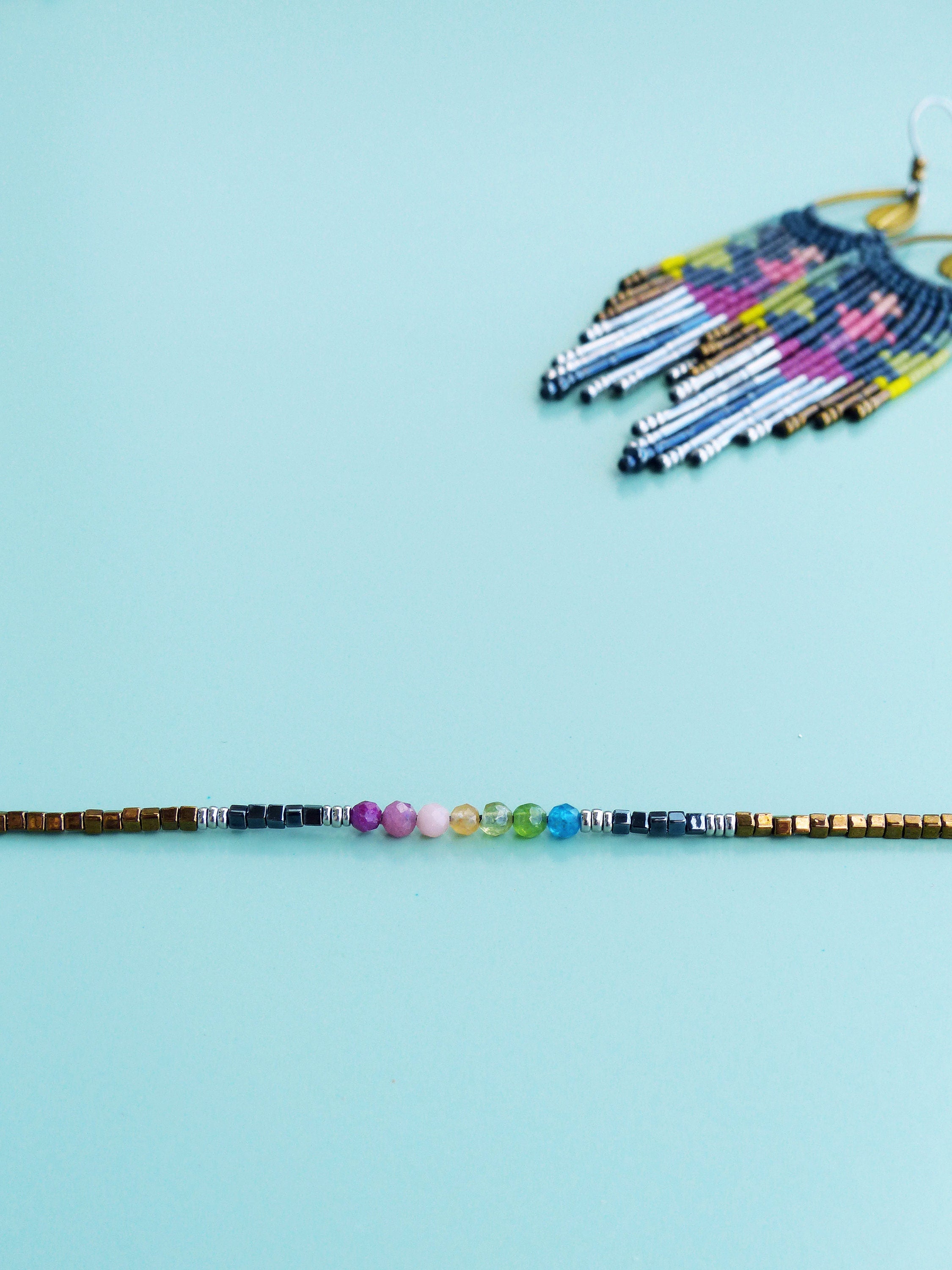 Peut inclure: Un bracelet en pierres précieuses arc-en-ciel avec des perles dorées et argentées. Le bracelet présente une variété de pierres précieuses colorées, notamment du rose, du jaune, du vert et du bleu.