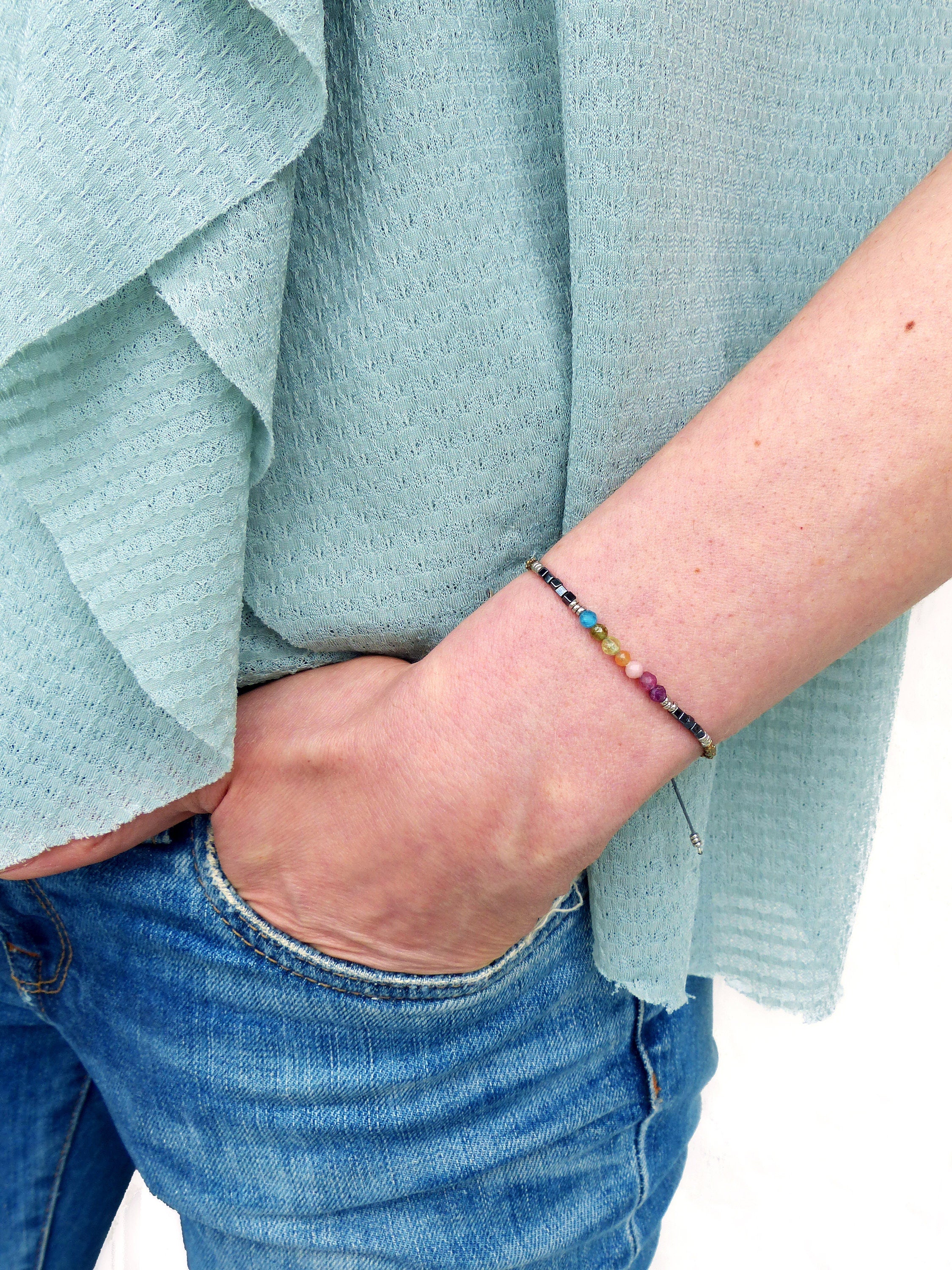 Peut inclure: Un bracelet coloré en perles avec un cordon argenté et une perle argentée à l'extrémité. Le bracelet est porté au poignet.