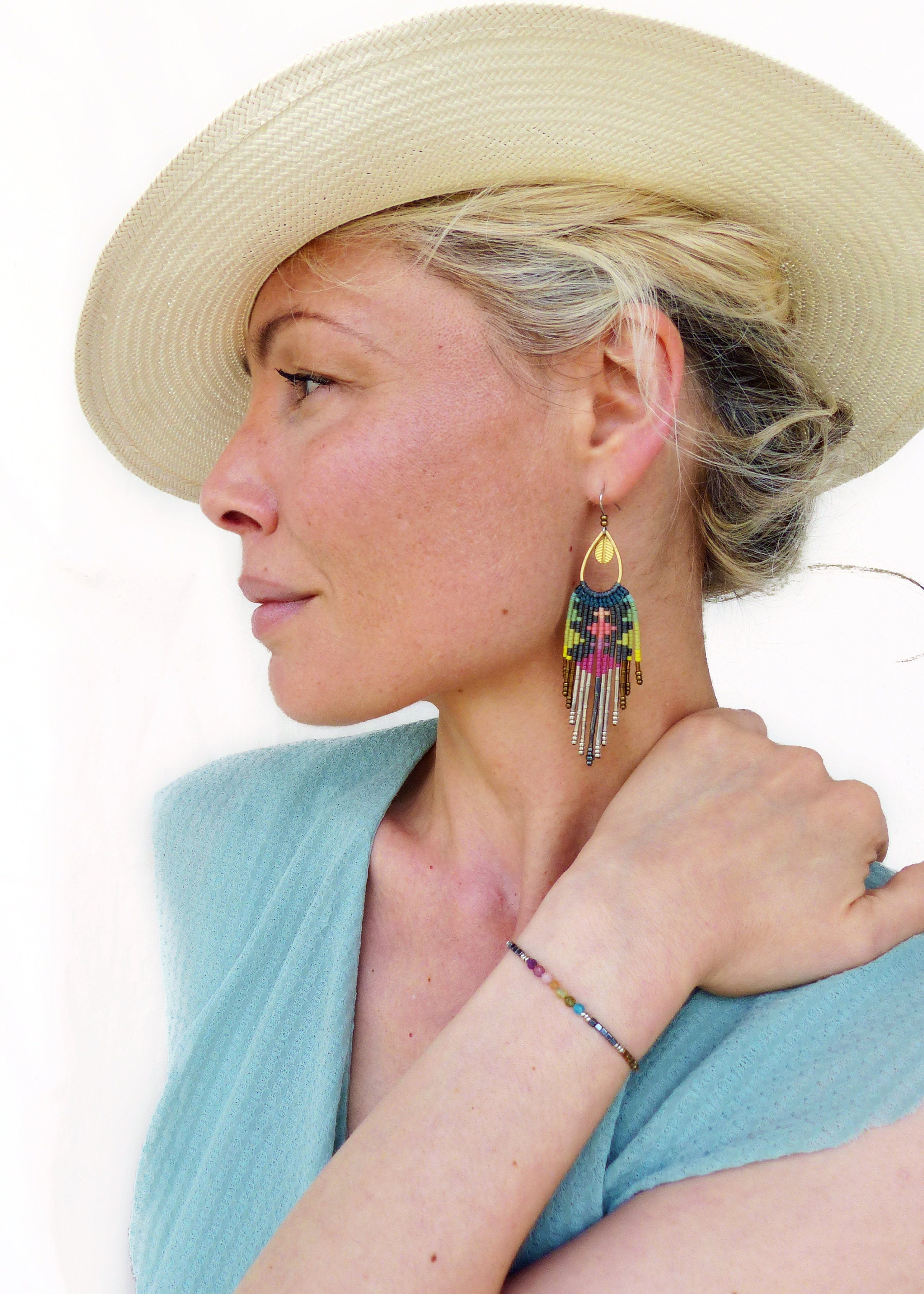 Peut inclure: Une femme portant un chapeau de paille et un haut turquoise avec un bracelet en perles colorées et de longues boucles d'oreilles en perles. 