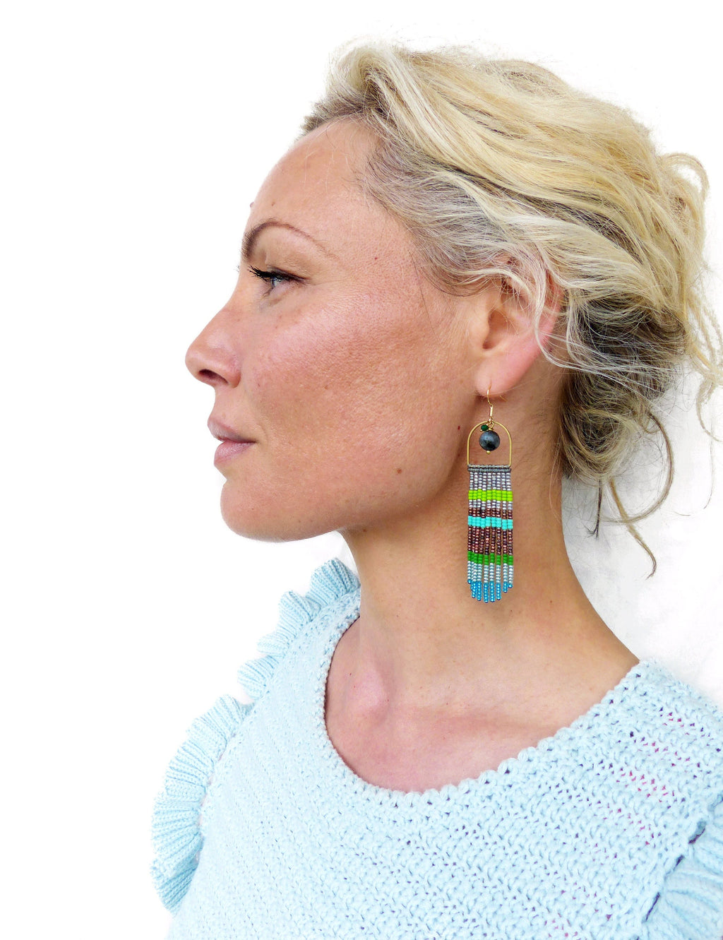 Peut inclure: Une femme portant un pull bleu clair avec une paire de longues boucles d'oreilles en perles colorées. Les boucles d'oreilles sont faites de petites perles colorées et ont un anneau en métal doré en haut.