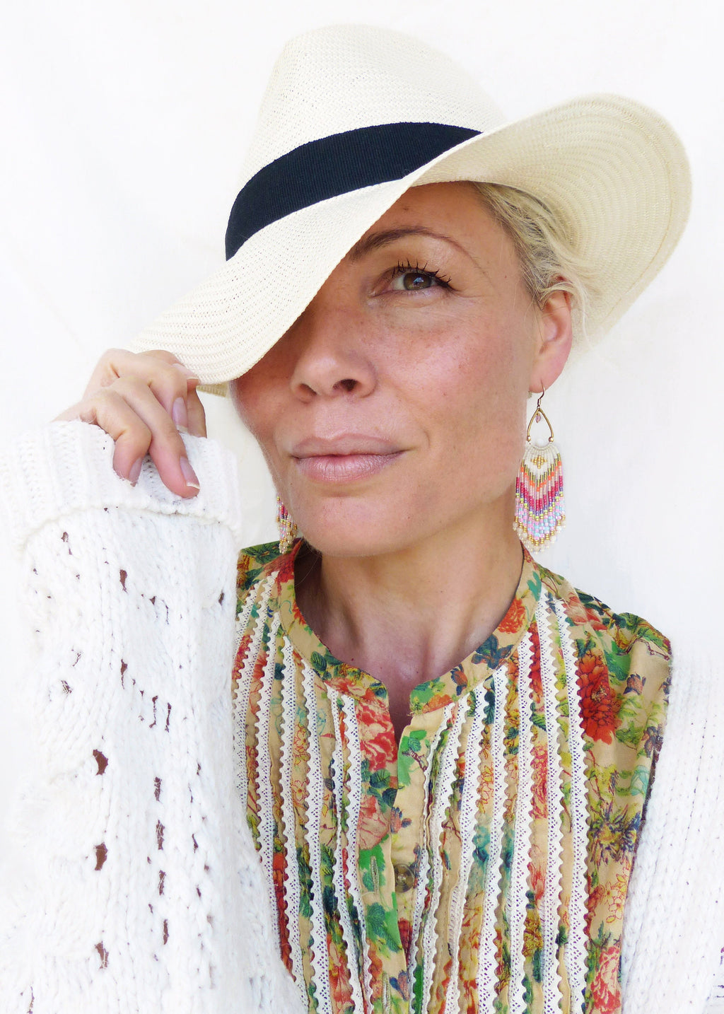 Peut inclure: Une femme portant un cardigan en crochet blanc, une blouse à imprimé floral avec des bordures en dentelle blanche et un chapeau de paille blanc avec un bandeau noir. Elle porte de longues boucles d'oreilles en perles colorées.