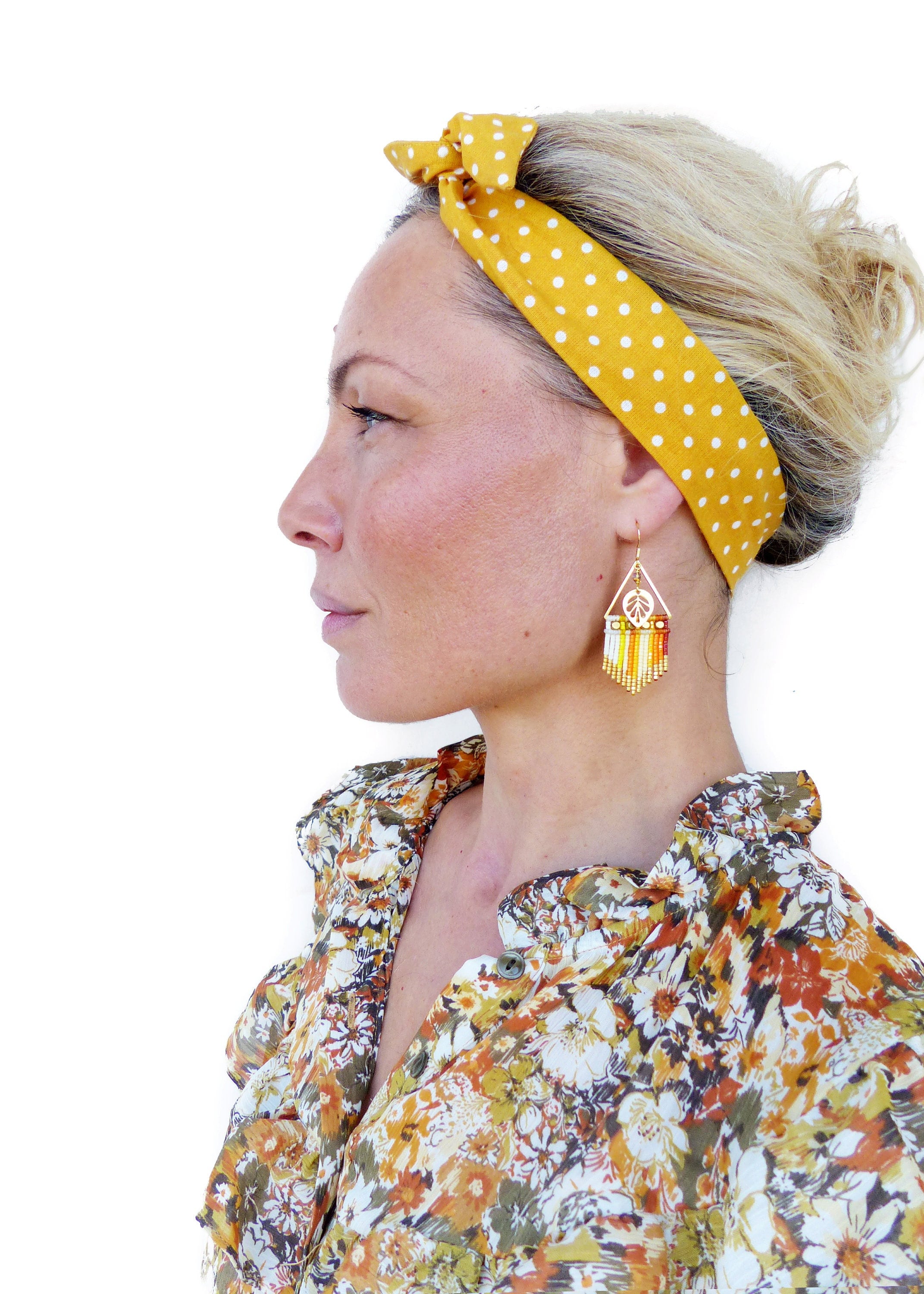 Peut inclure: Une femme aux cheveux blonds porte un bandeau jaune à pois blancs et une chemise à imprimé floral. Elle porte de longues boucles d'oreilles en perles avec un motif de feuille d'or.