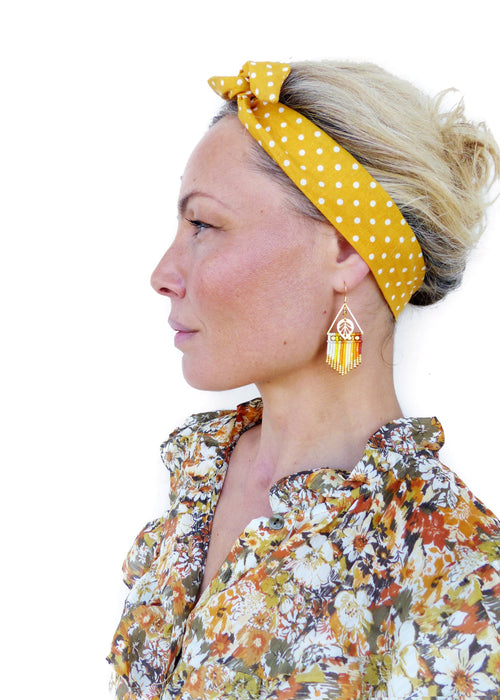 Peut inclure: Une femme aux cheveux blonds porte un bandeau jaune à pois blancs et une chemise à imprimé floral. Elle porte de longues boucles d'oreilles en perles avec un motif de feuille d'or.
